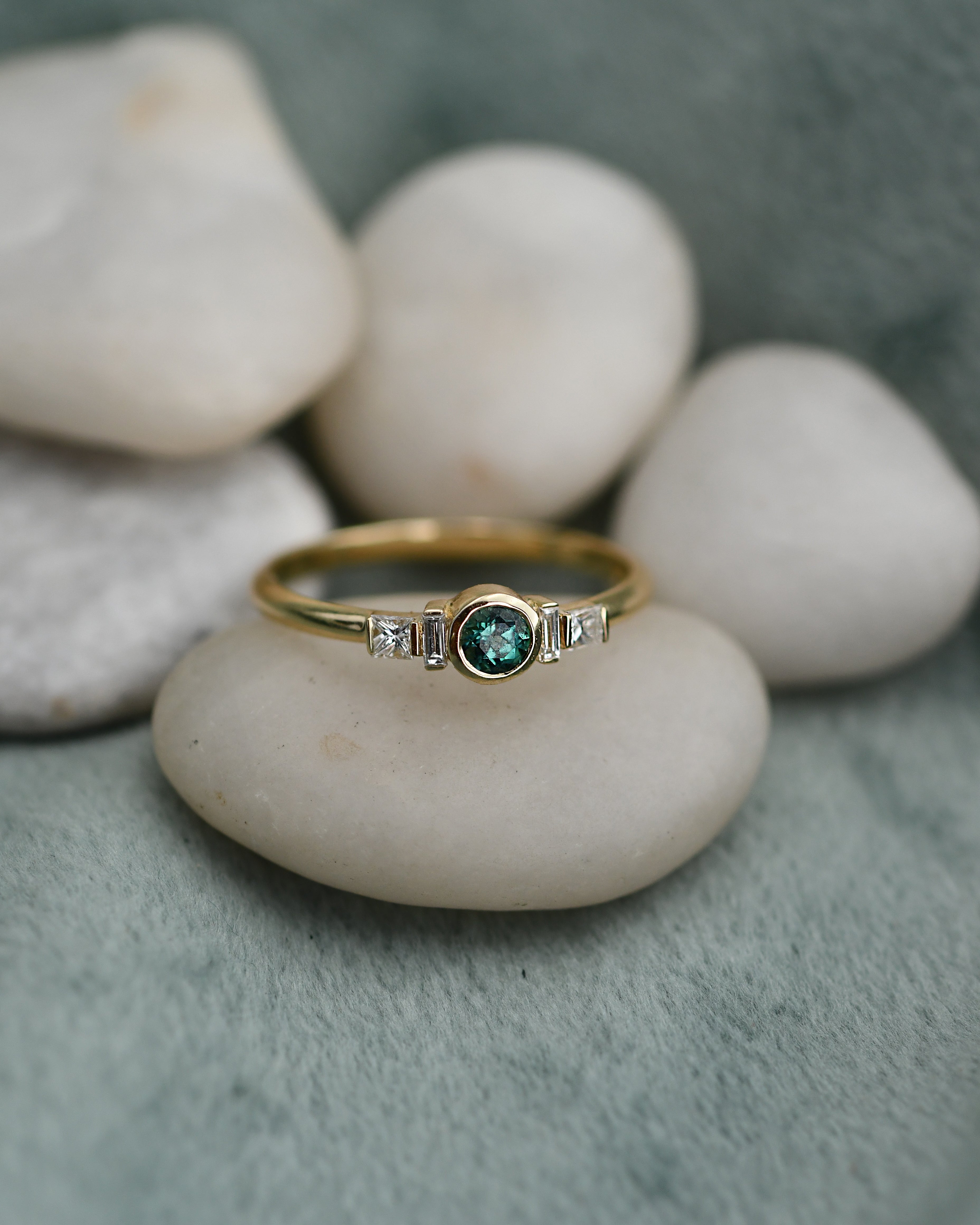 A gold ring with a round green emerald-cut center stone and small clear side white diamonds