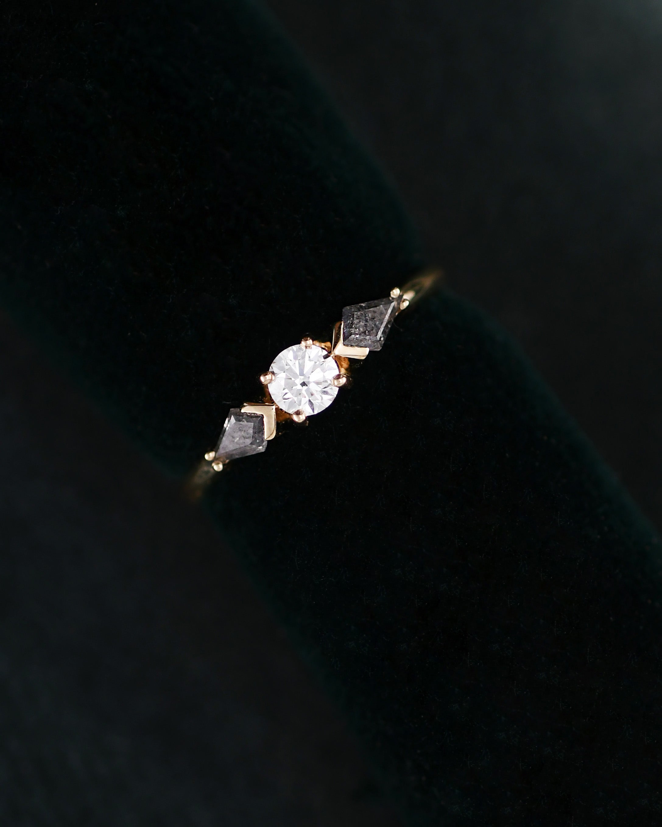 A three stone diamonds ring with a round center white diamond and two kite-cut side grey diamonds