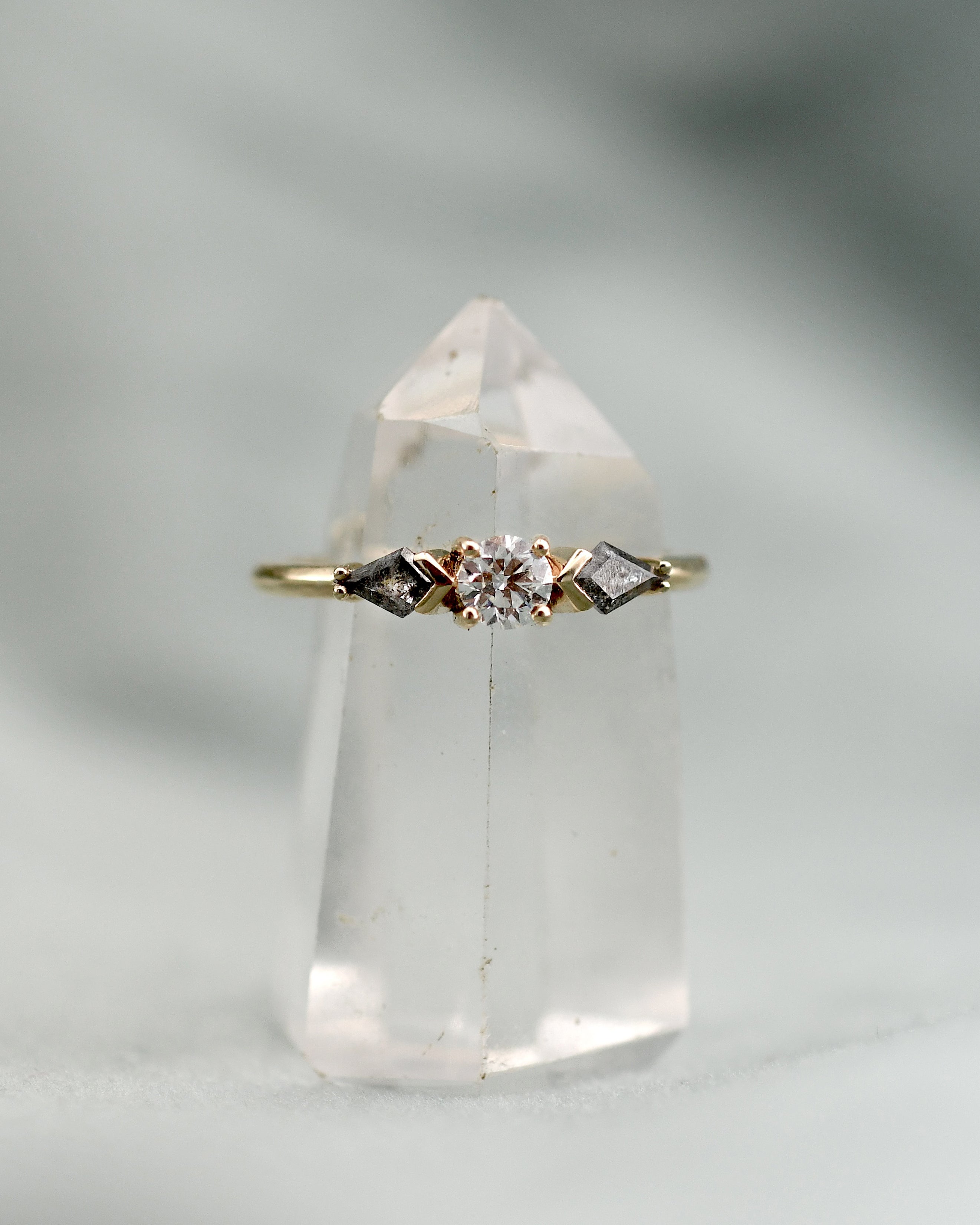A delicate gold ring with a central clear white diamond and two grey kite -cut diamonds 