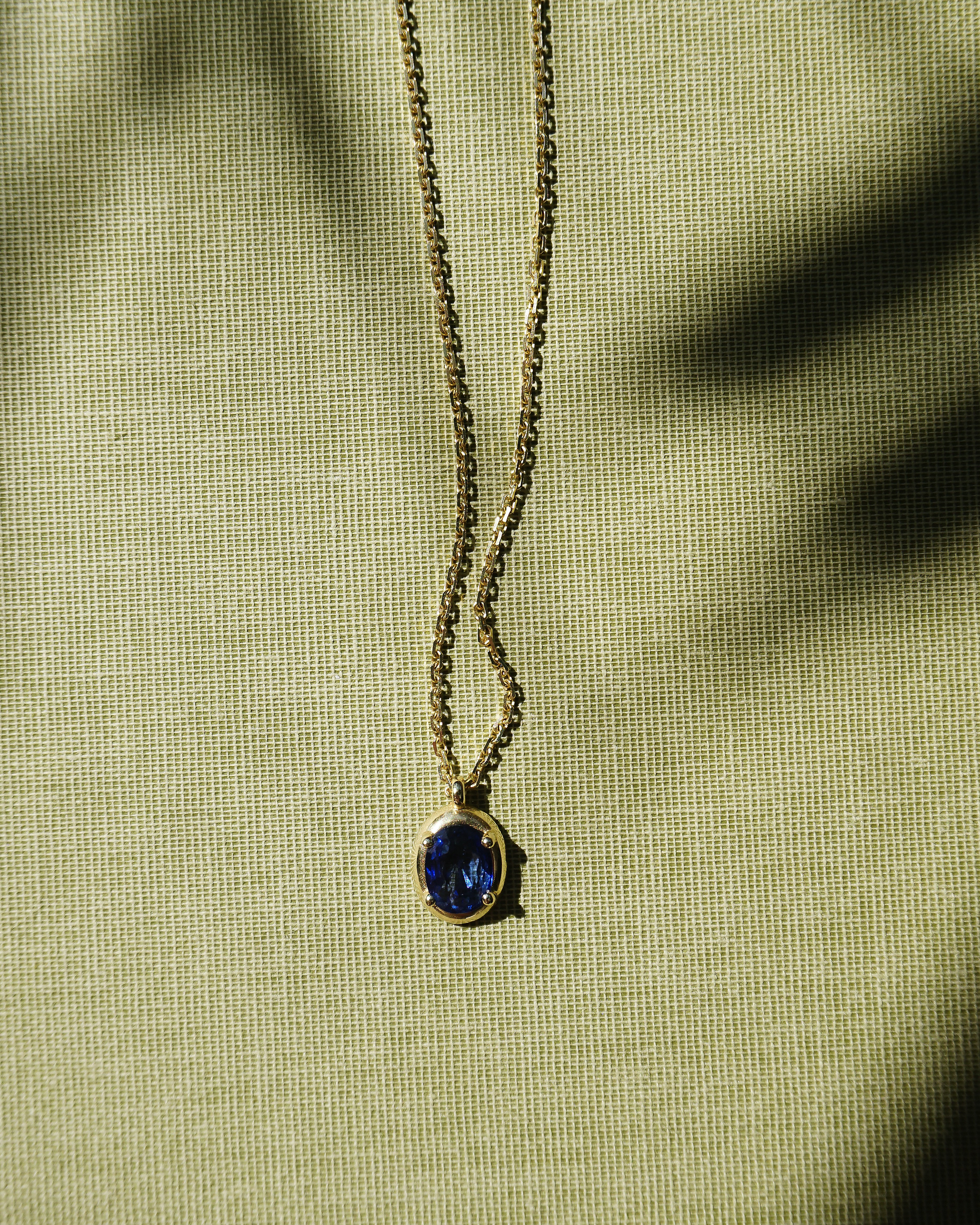 Necklace with a blue pendant on a green fabric background