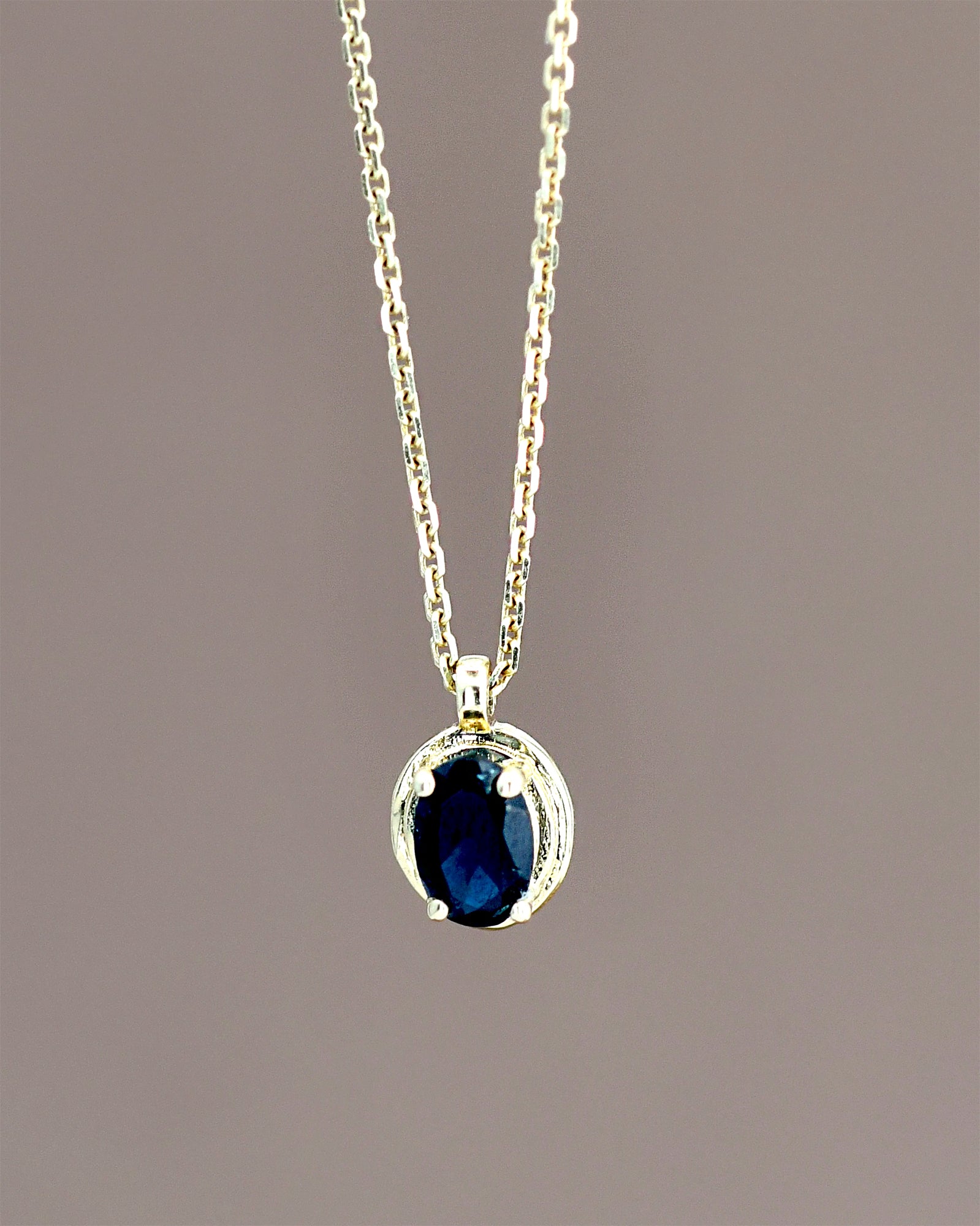 Gold necklace with a blue gemstone pendant on a brown background