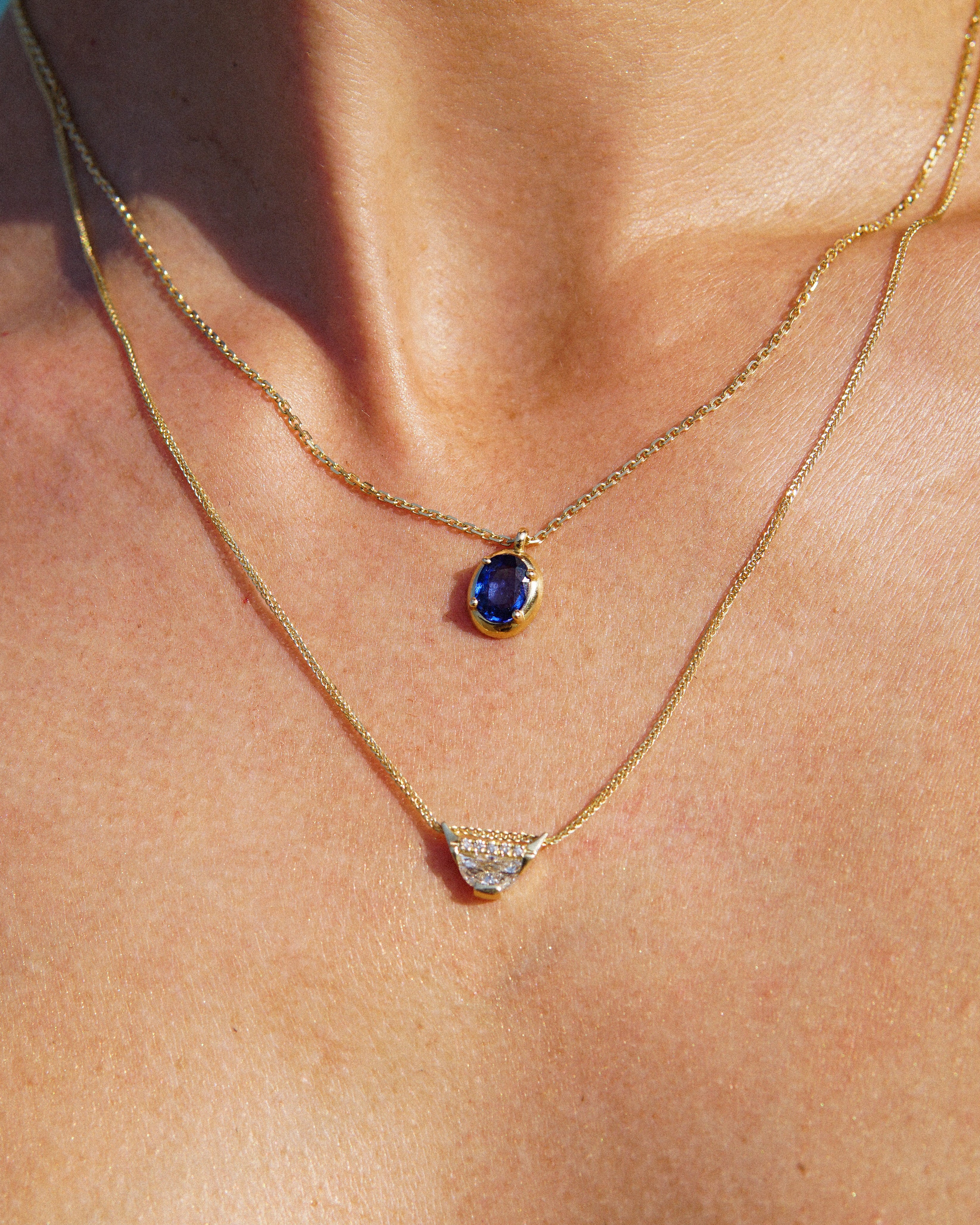 Close-up of a gold necklace with a blue gemstone pendant on a person's neck.