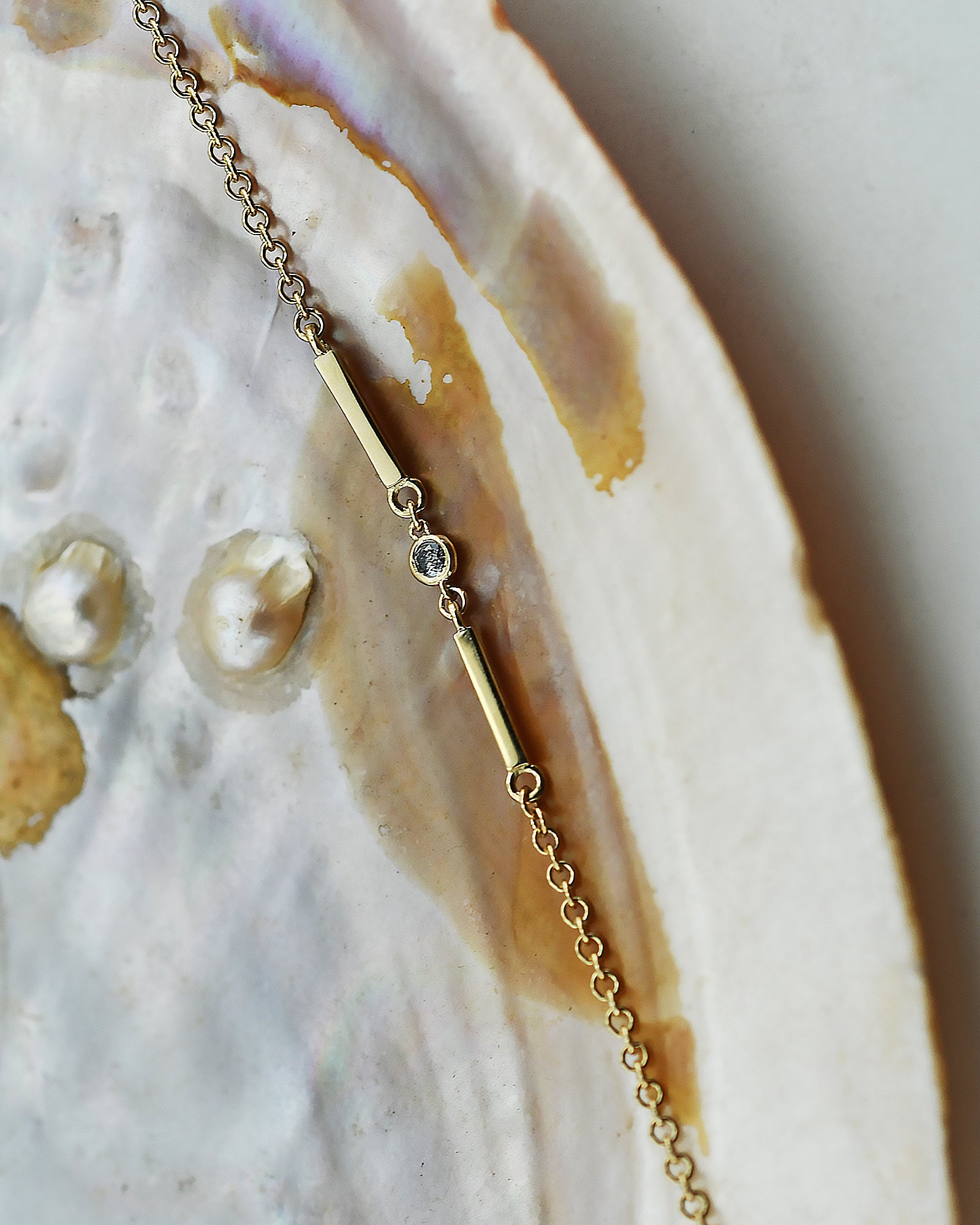 Gold bracelete with gray Diamond and two bars on a shell background