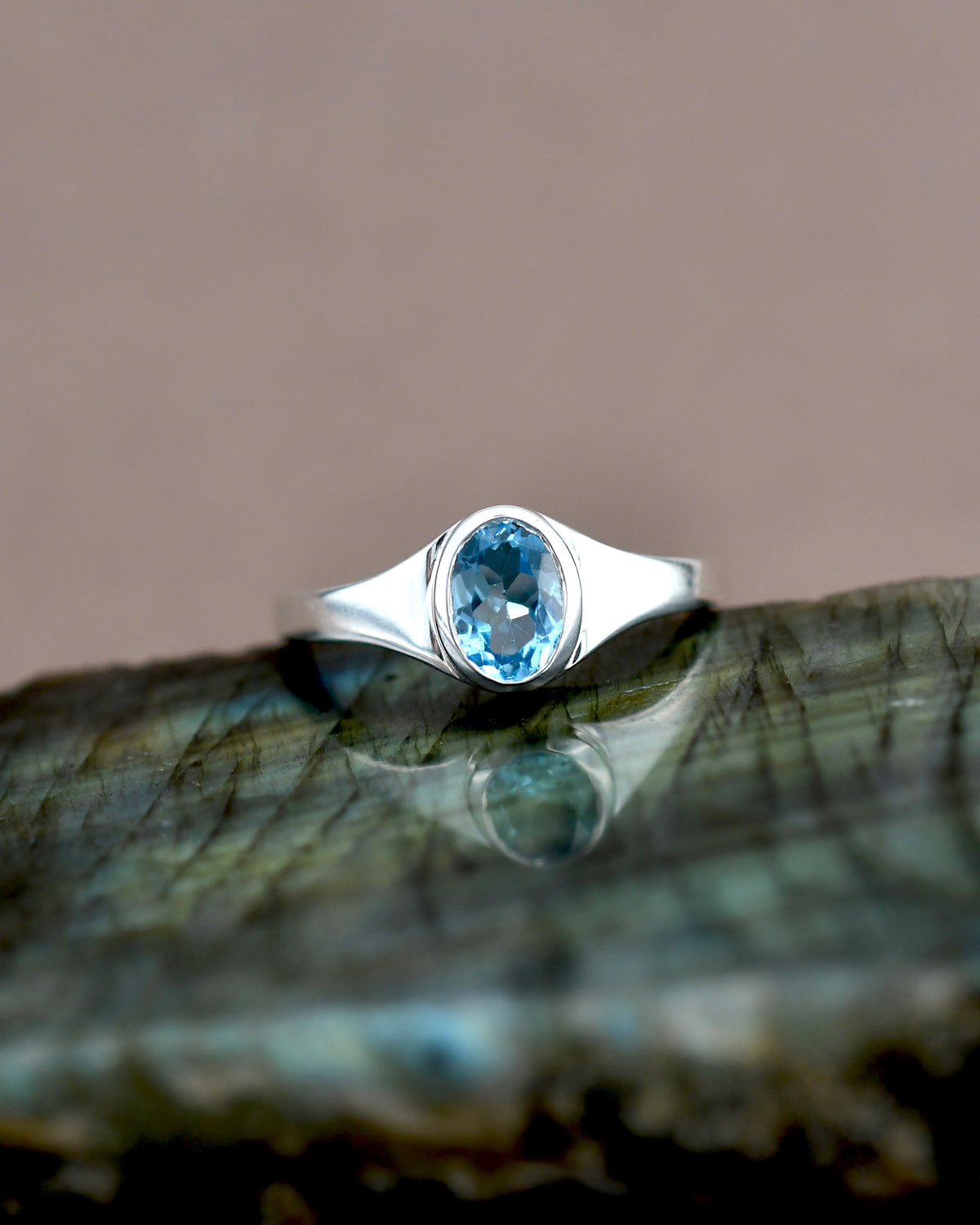 Silver ring with a blue gemstone on a reflective surface