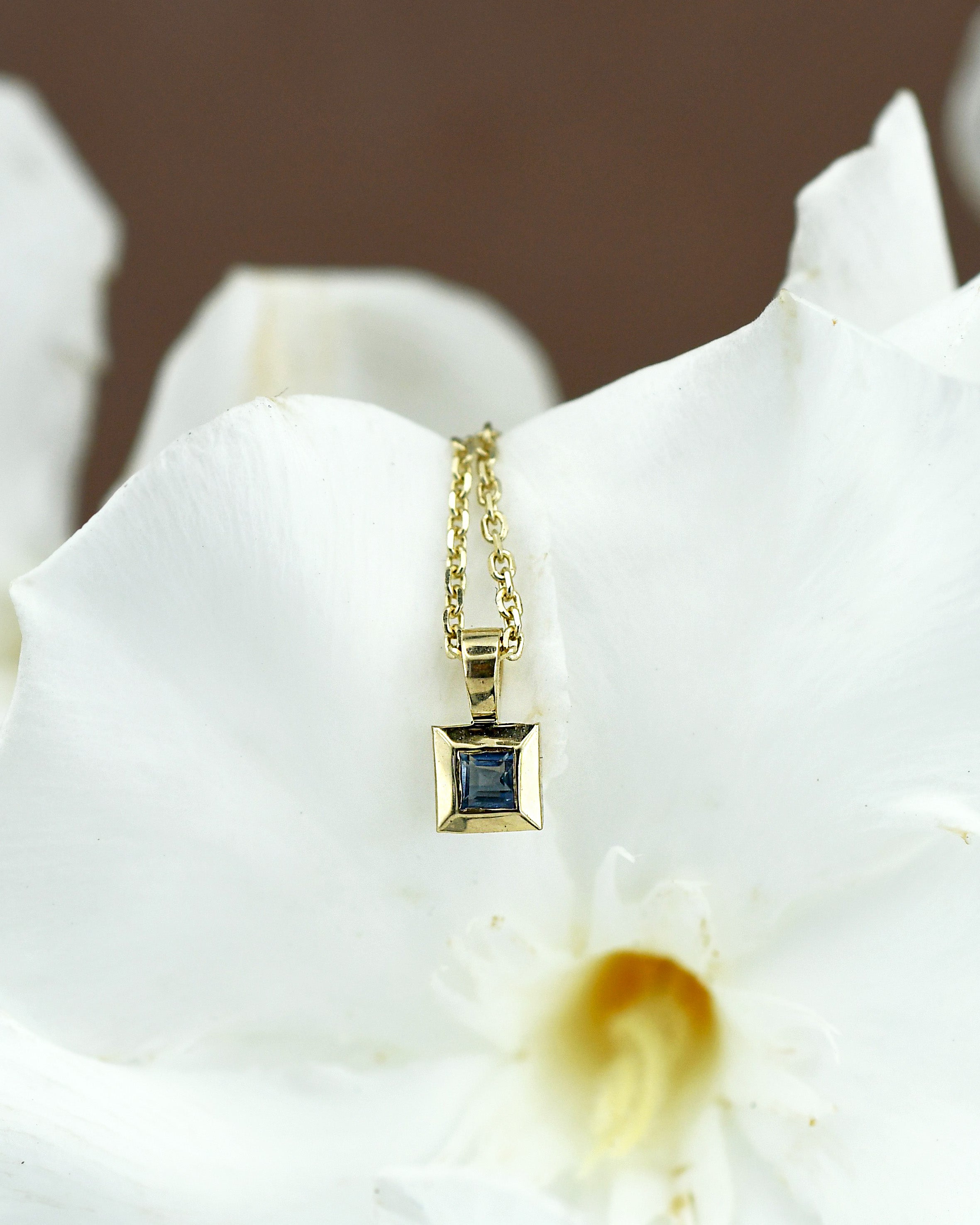 Gold necklace with a blue sapphire gemstone pendant on a white flower background