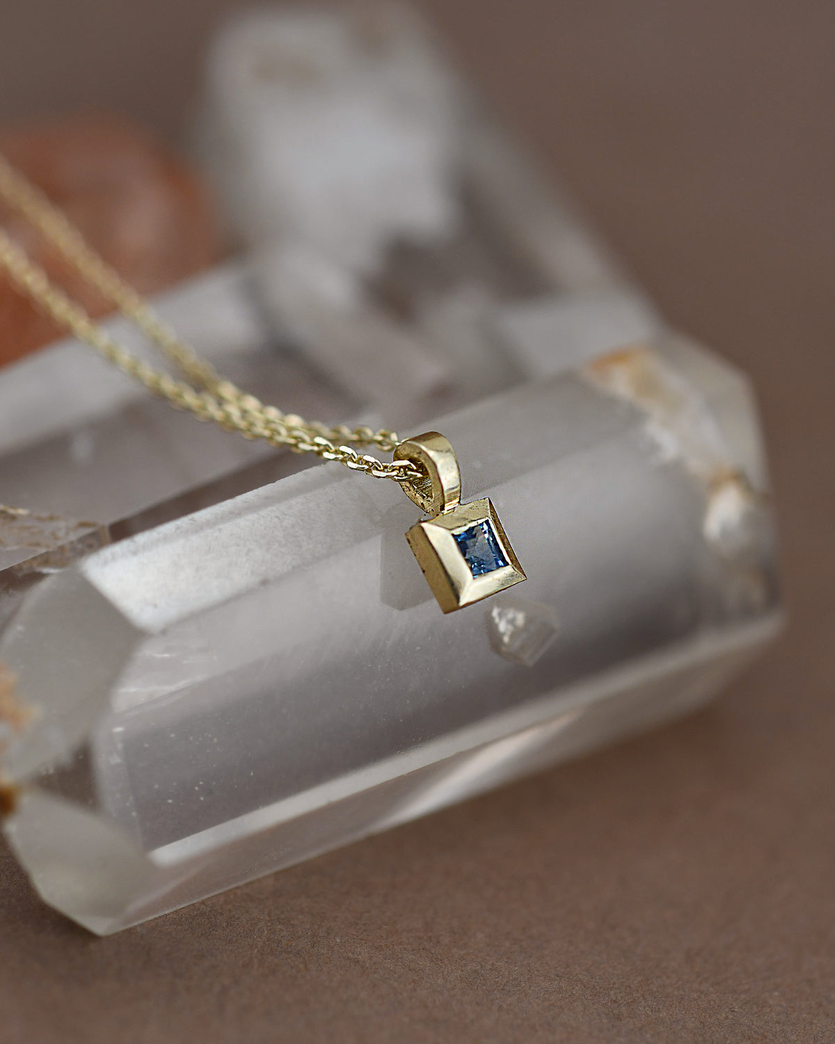 Gold necklace with a blue gemstone pendant on a crystal background