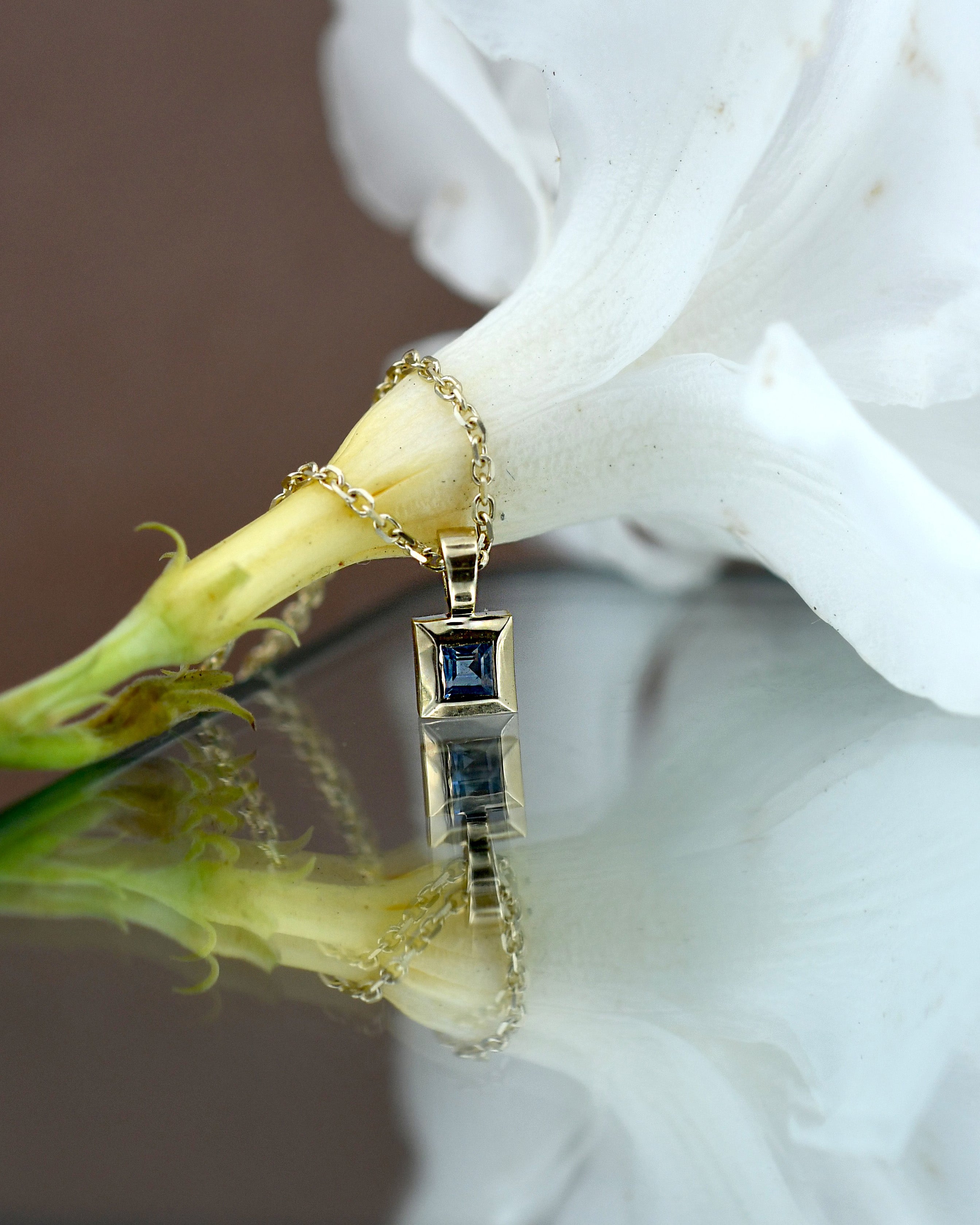 Gold pendant with a blue sapphire gemstone on a white flower