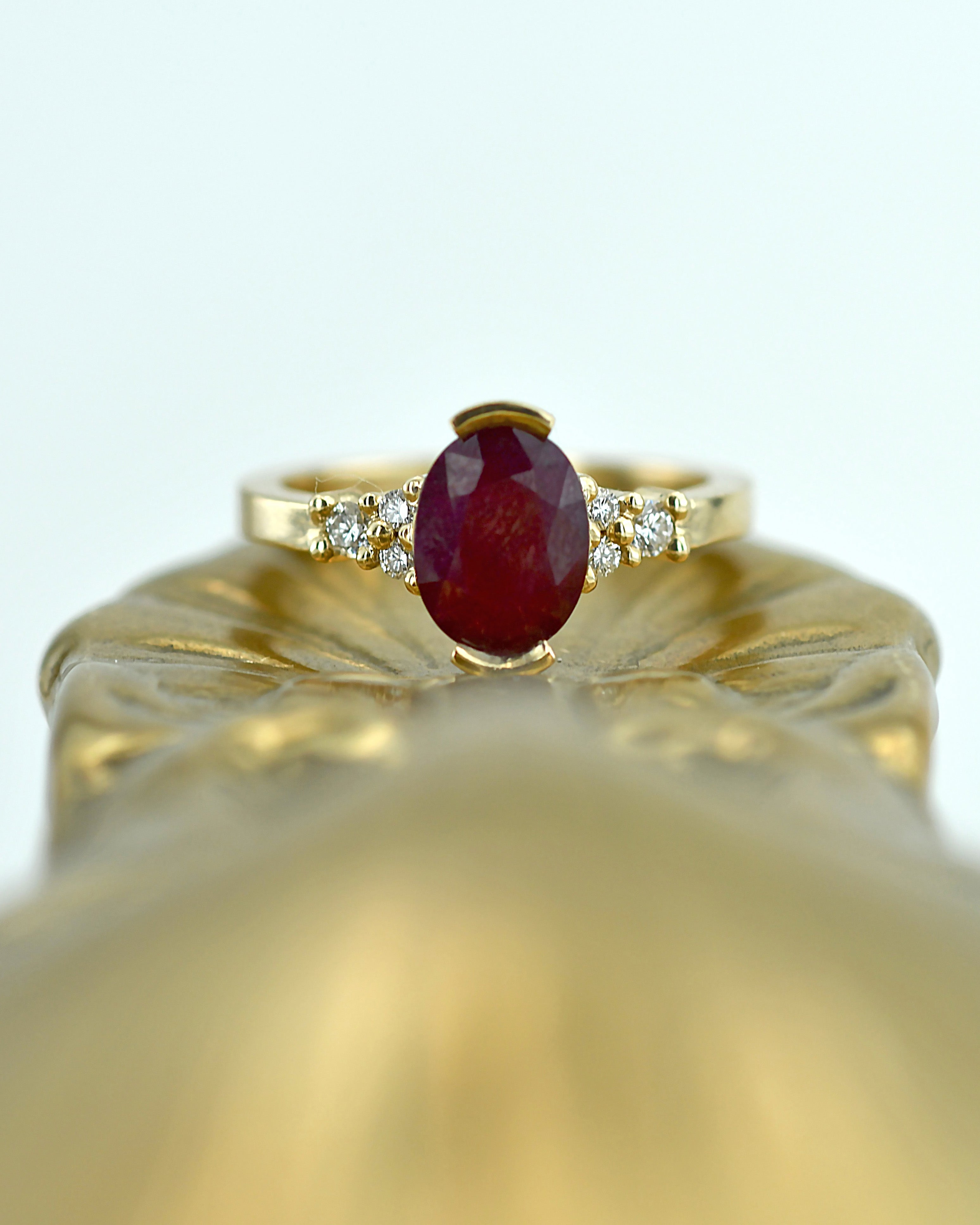 Gold ring with a ruby gemstone and small diamonds on a light gray background