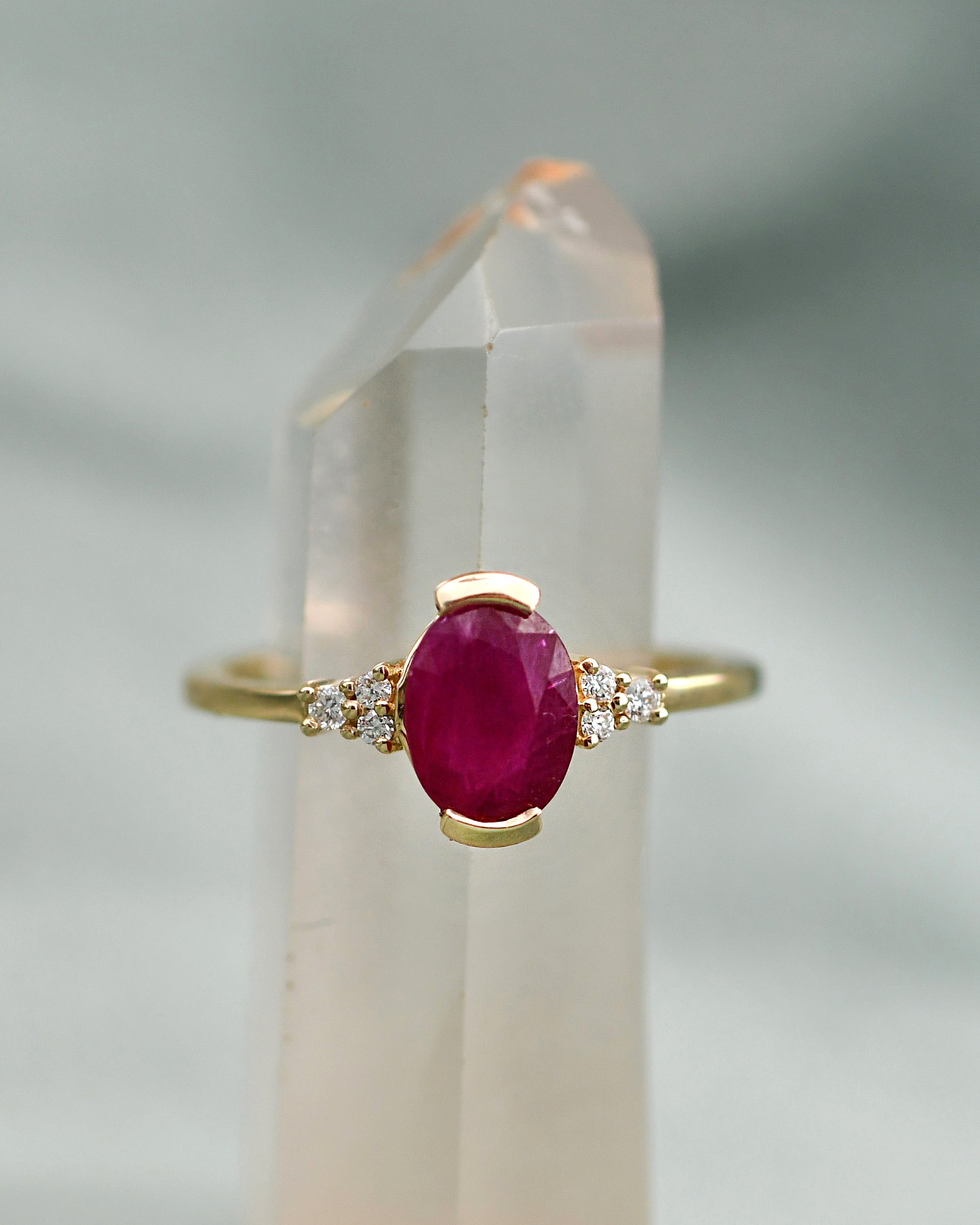 A gold ring with an oval-cut deep red center ruby gem stone and small white diamonds on either side,