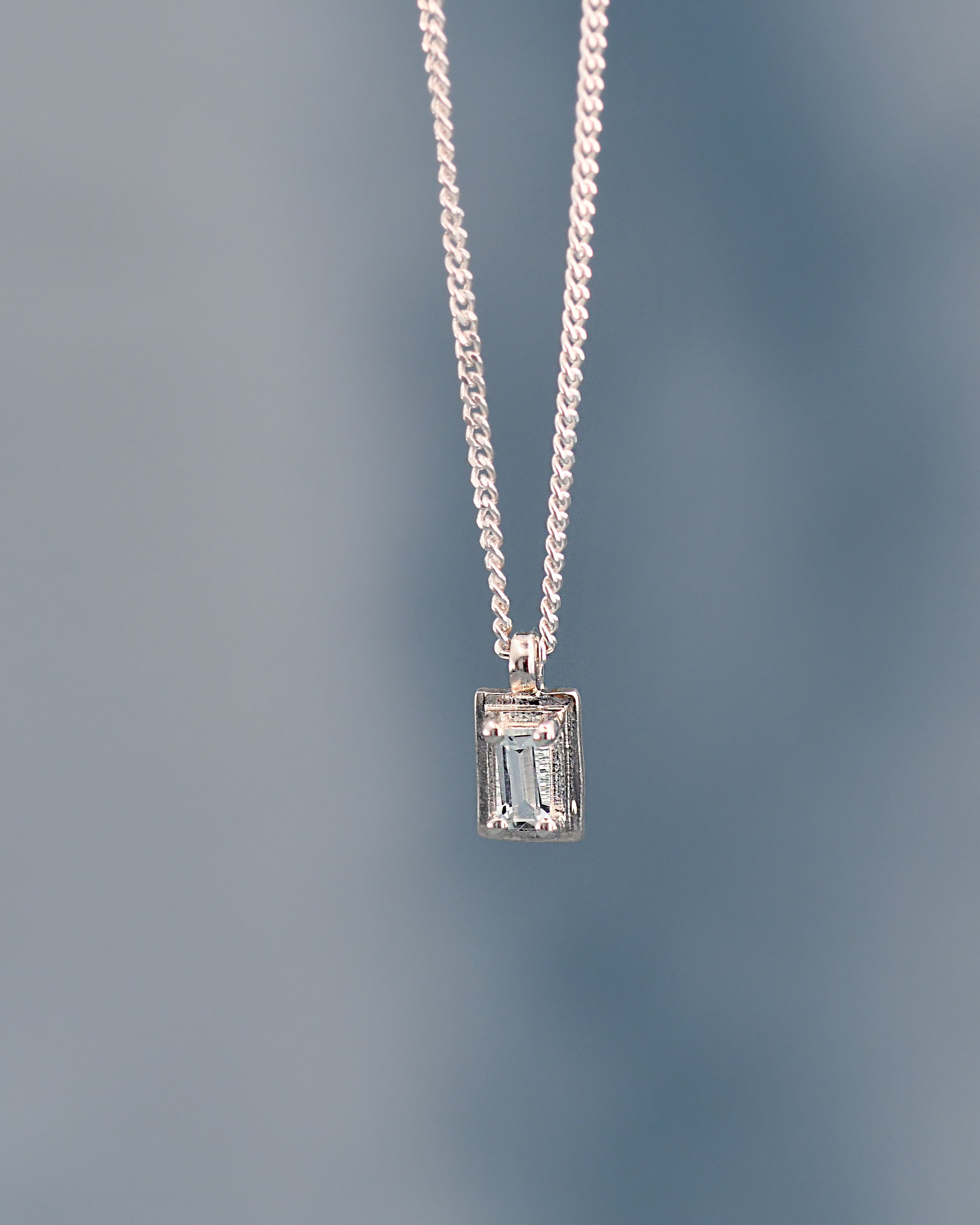 Silver necklace with a rectangular pendant on a gradient blue background