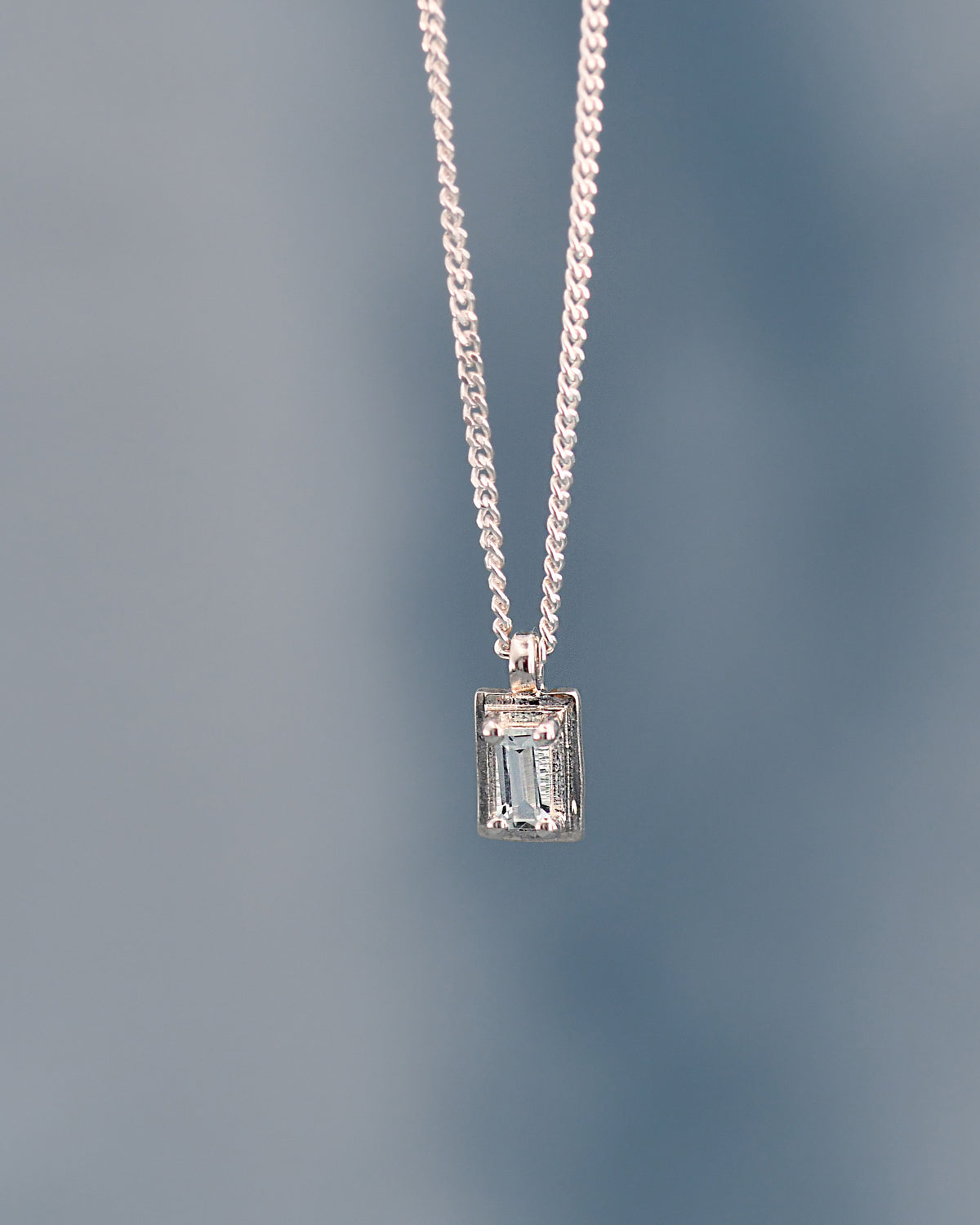 Silver necklace with a rectangular pendant on a gradient blue background