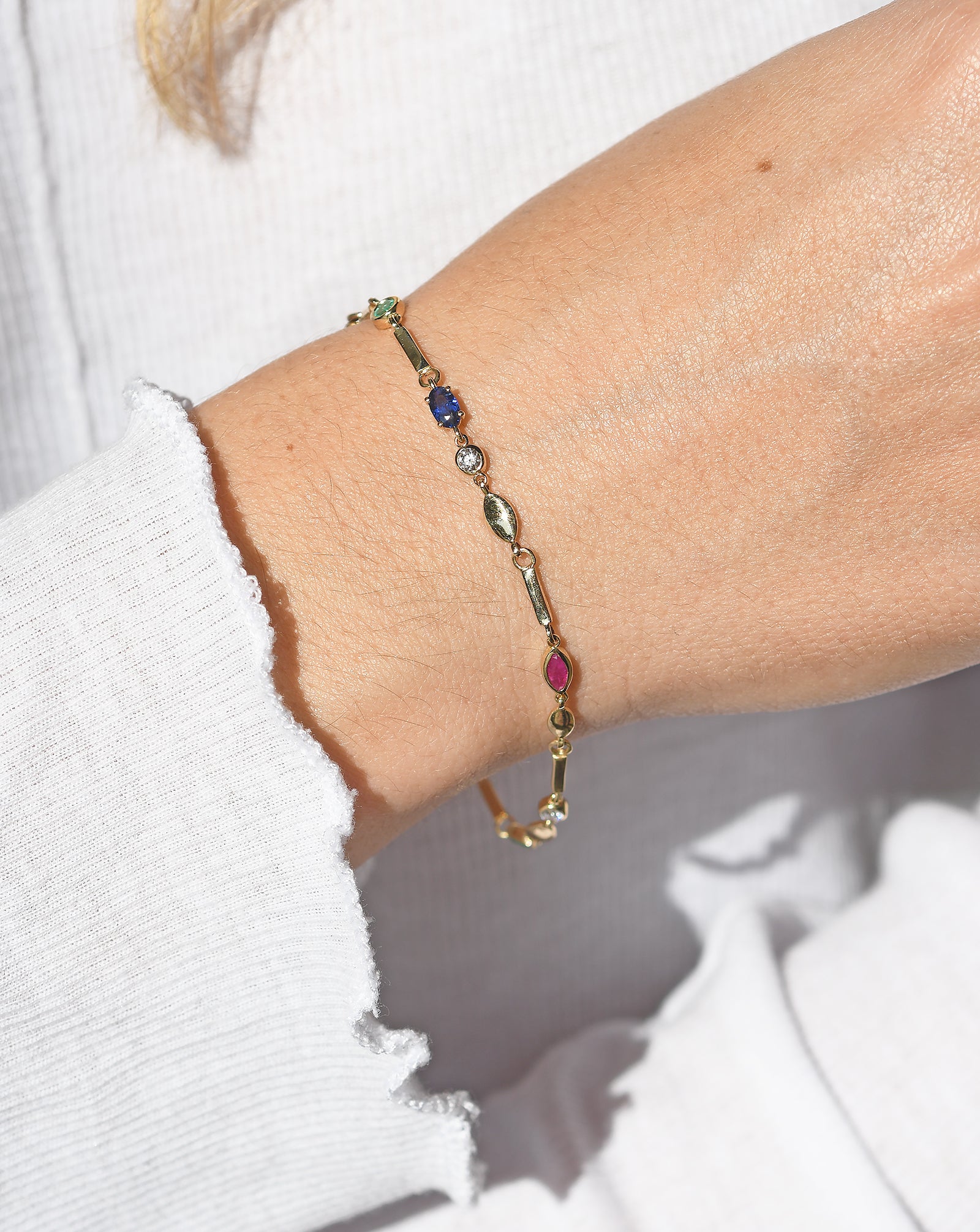 A gold bracelet with multicolored gemstones on a person's wrist.