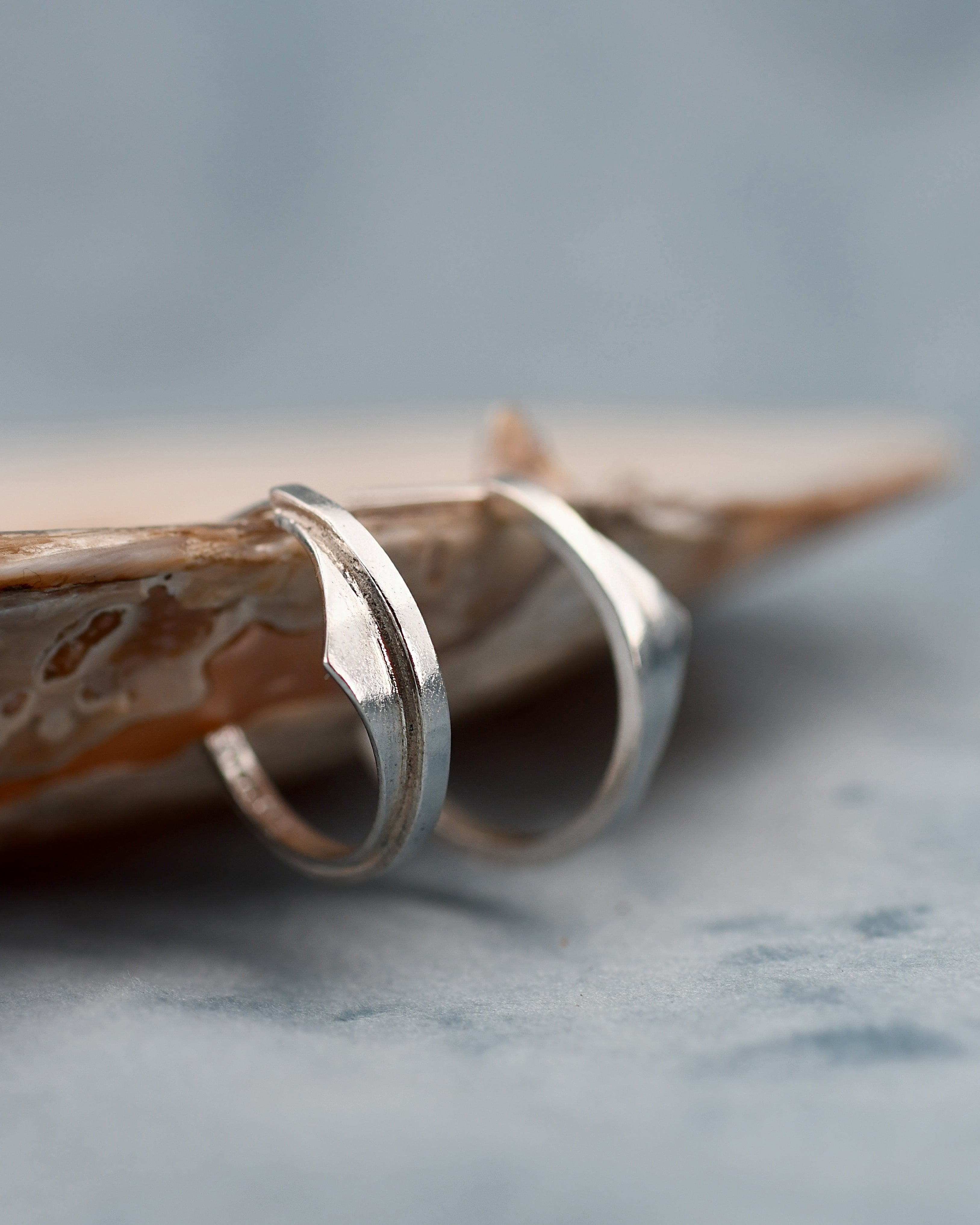 Two silver earrings on a textured surface with a blurred background
