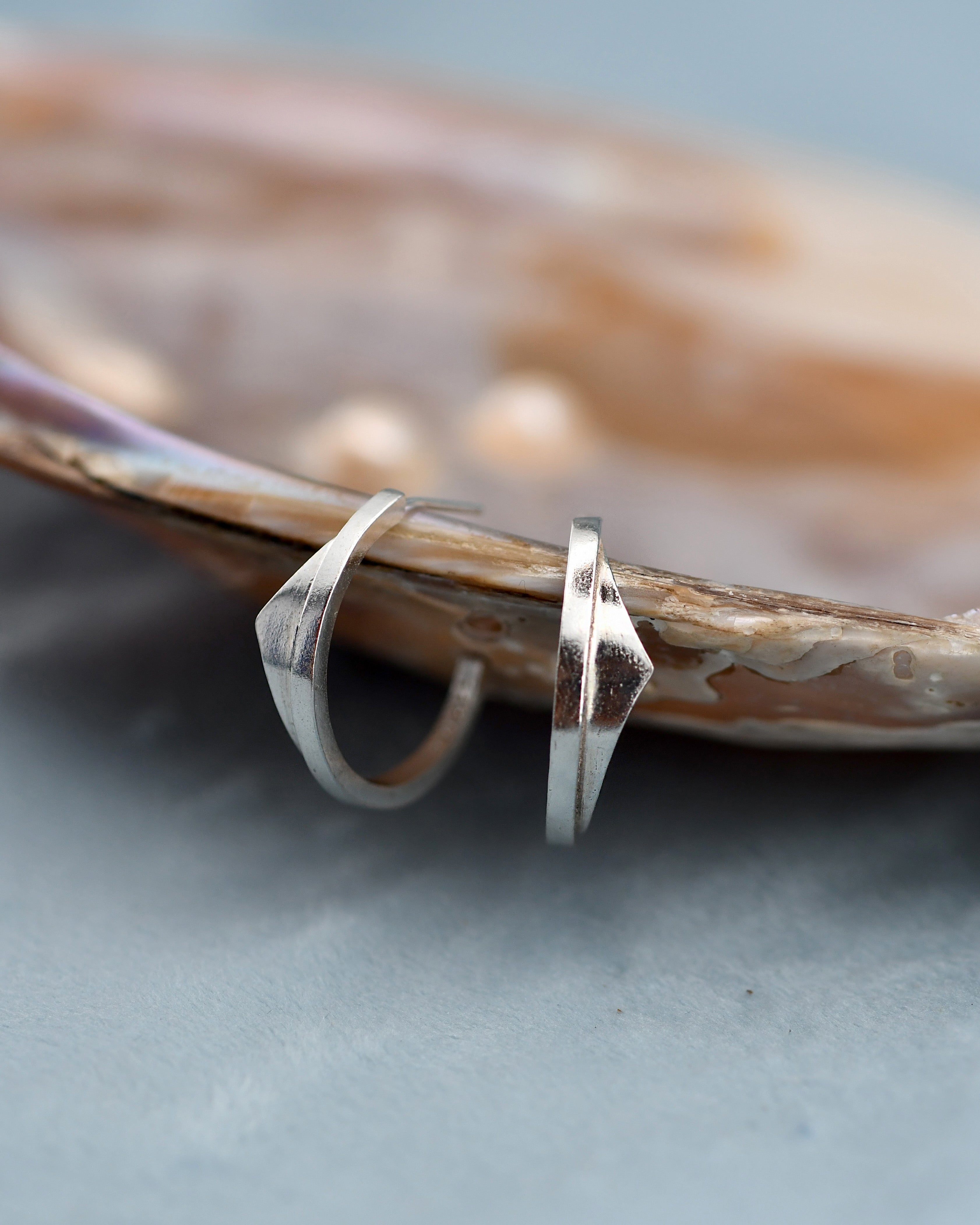 Silver hoop earrings on a textured surface with a shell in the background
