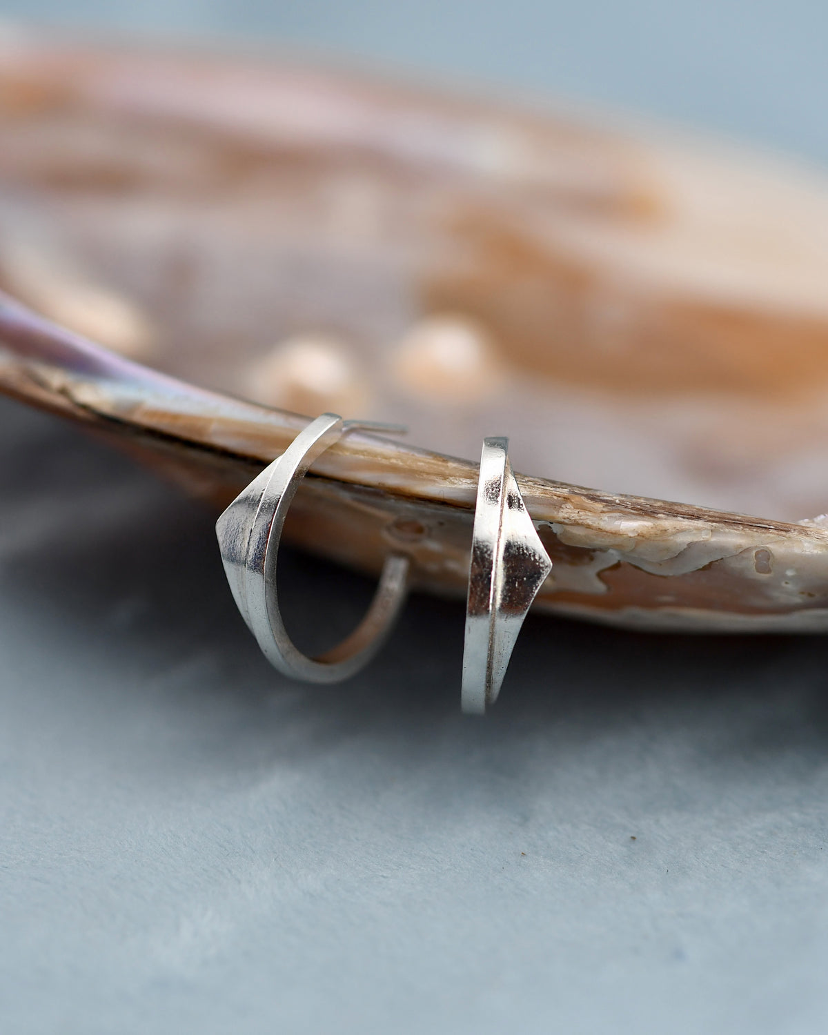 Silver hoop earrings on a textured surface with a shell in the background