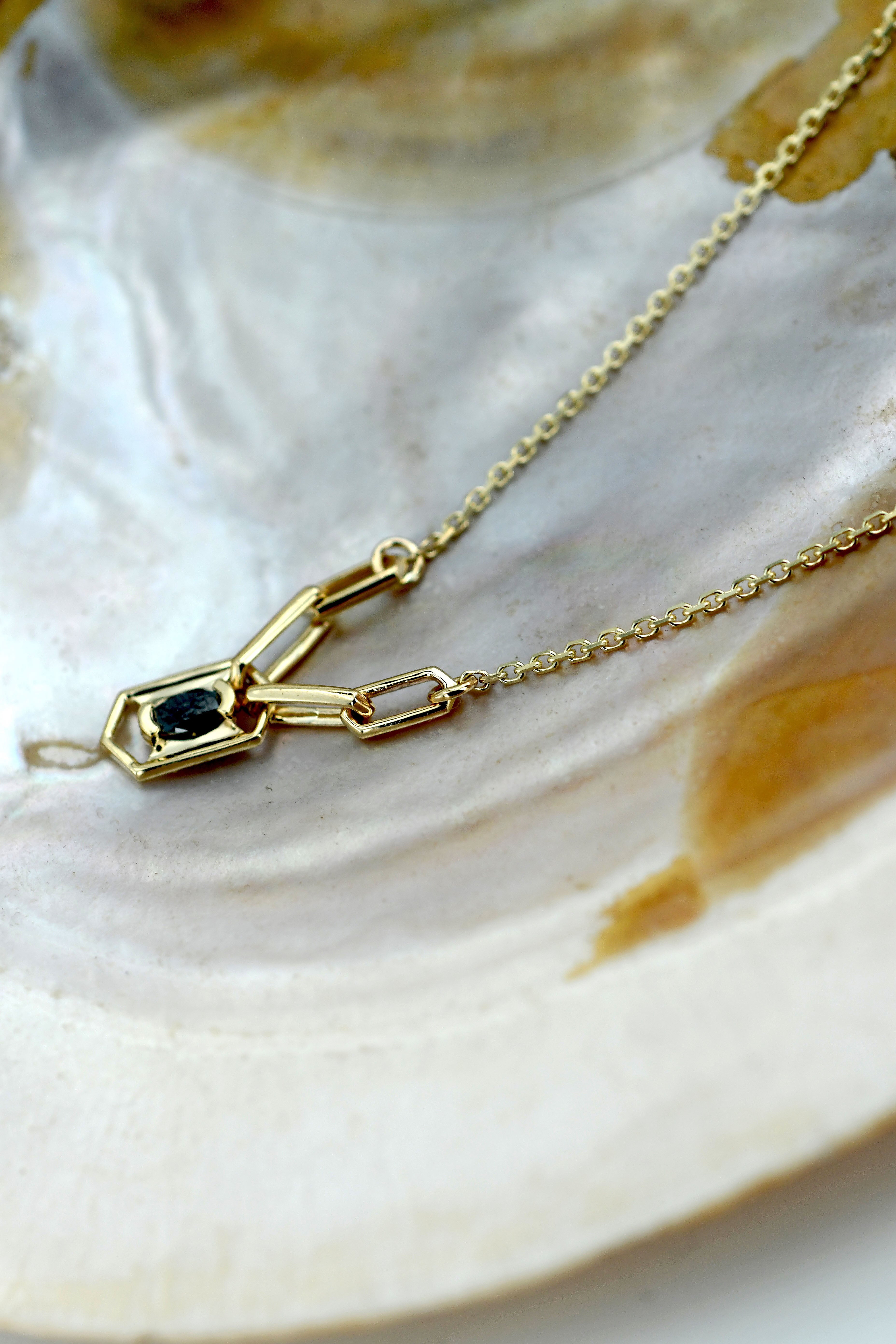 Gold necklace with a black diamond on a shell background