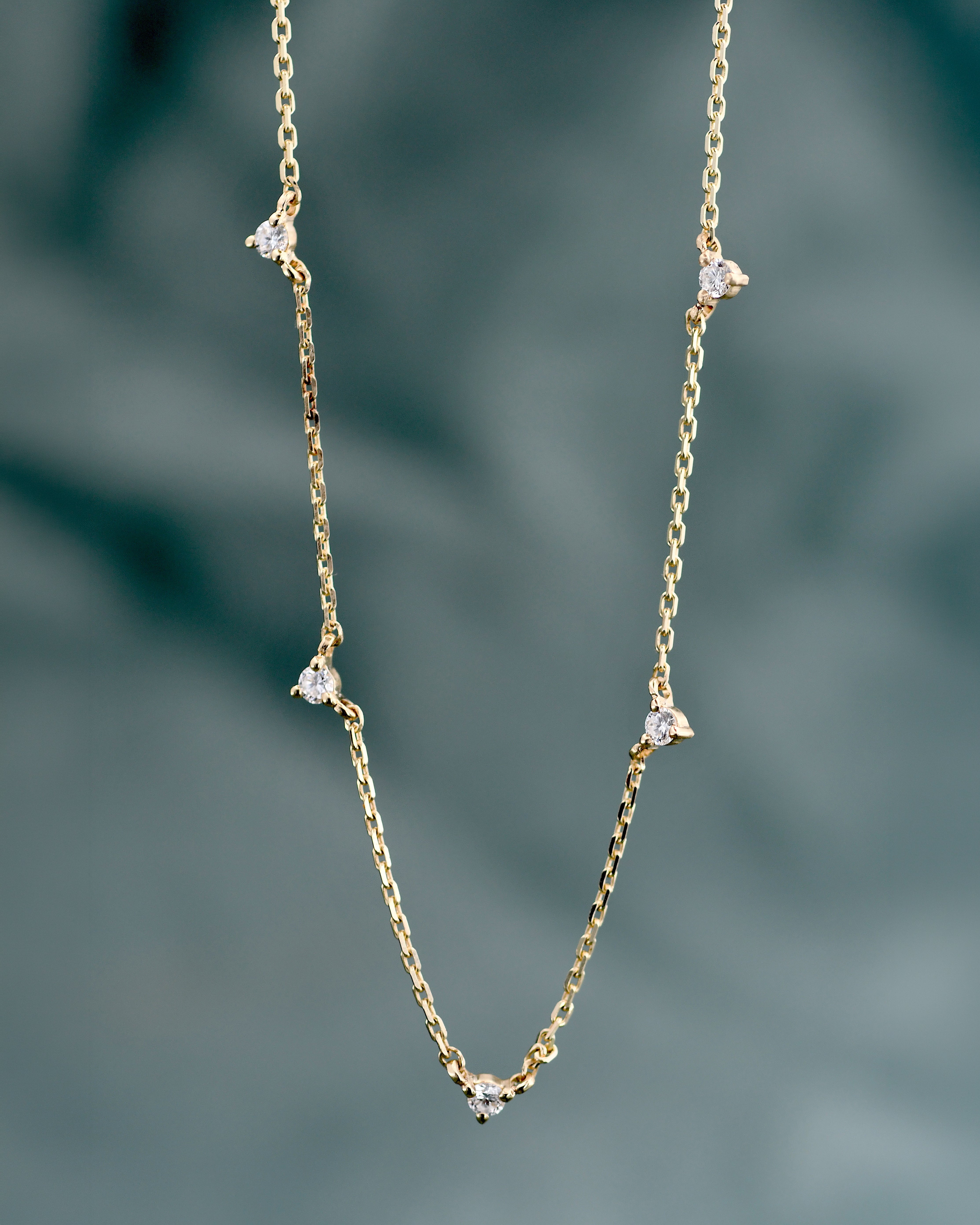 a gold chain necklace with five white diamonds