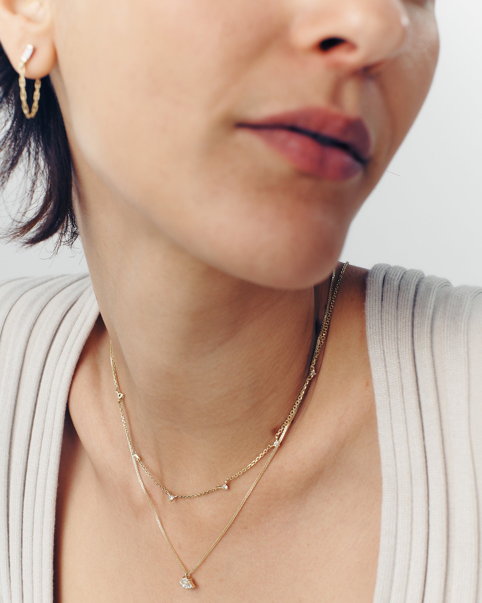 A close-up of a woman's neck wearing a gold chain necklace with five white diamonds, with the necklace extending below the clavicle.