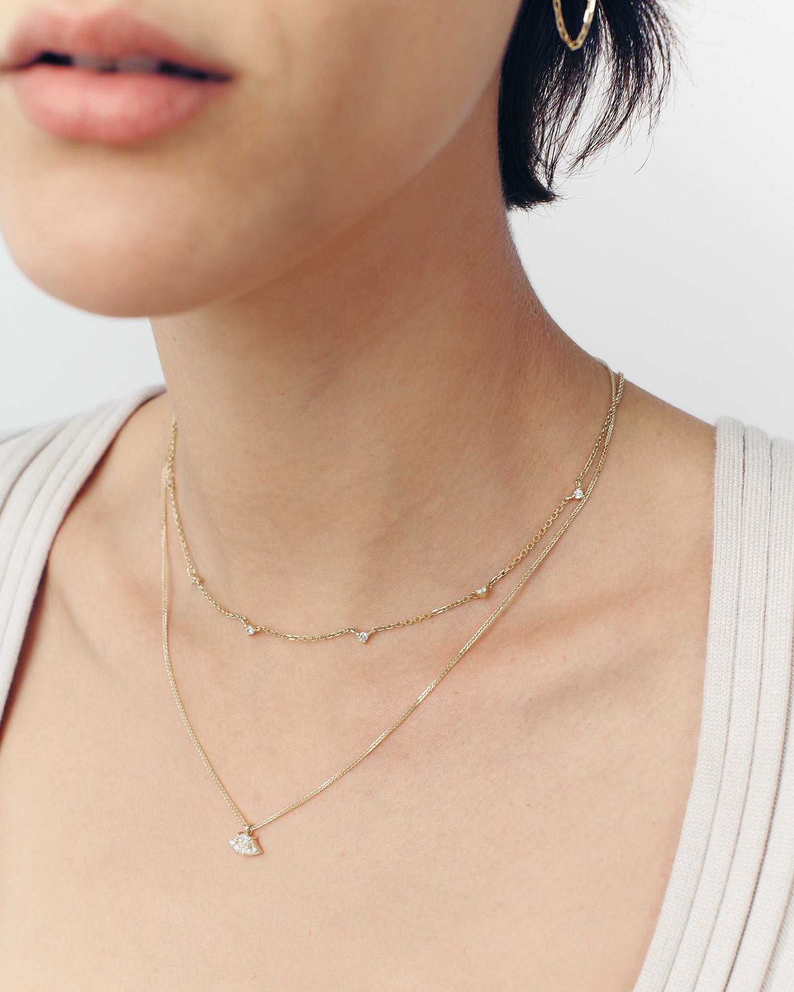 A close-up of a woman's neck wearing a gold chain necklace with five white diamonds, with the necklace extending below the clavicle.