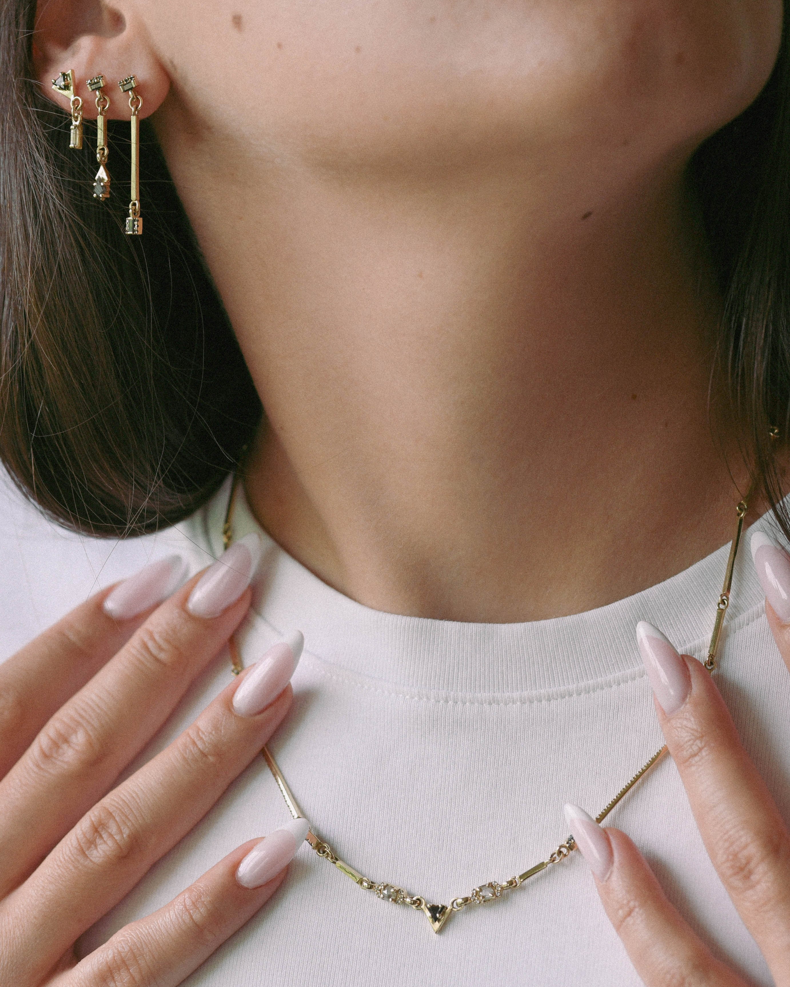 Close-up of a person wearing gold earrings and a necklace with a white background