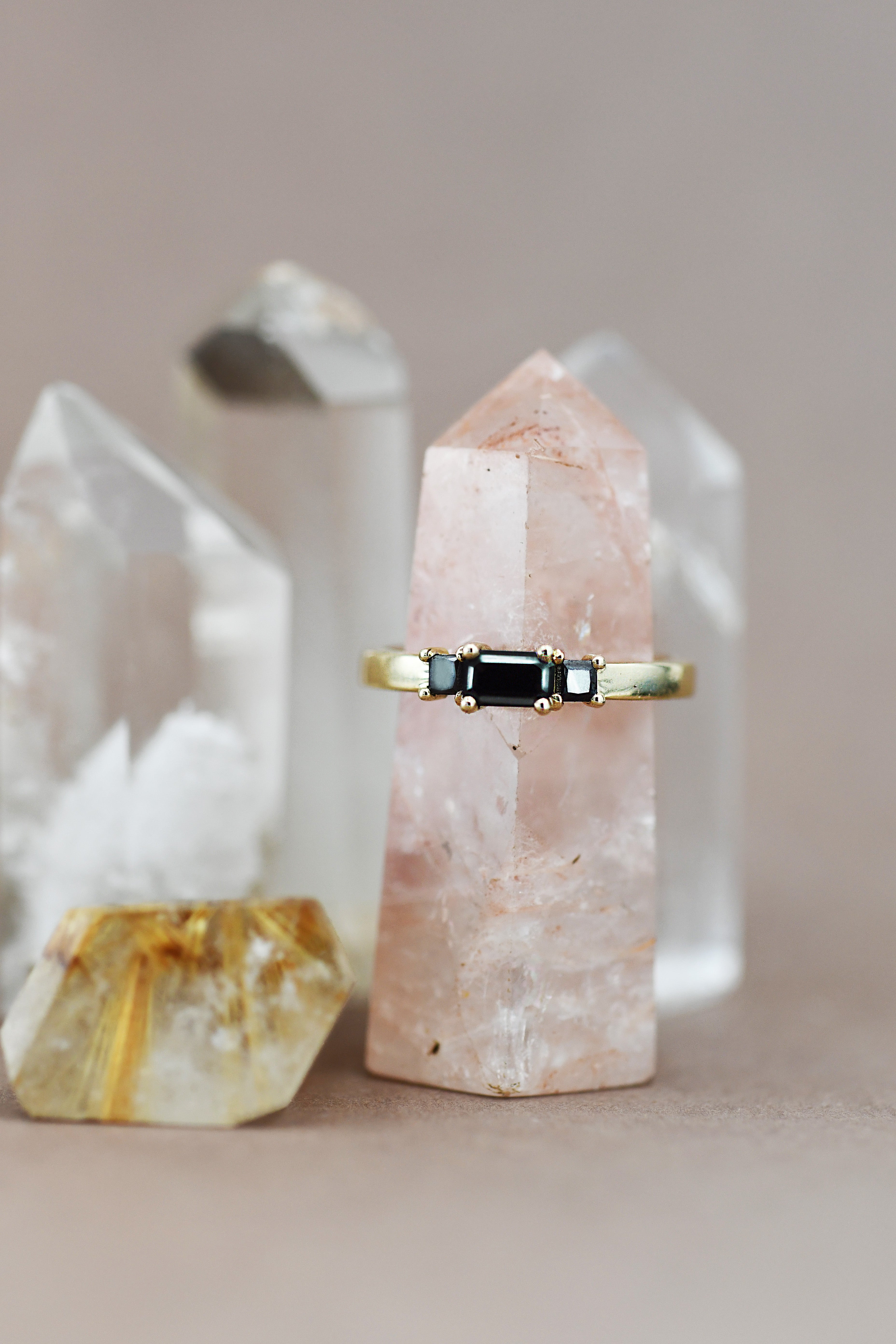 Gold ring with a black gemstone on a pink crystal with a neutral background