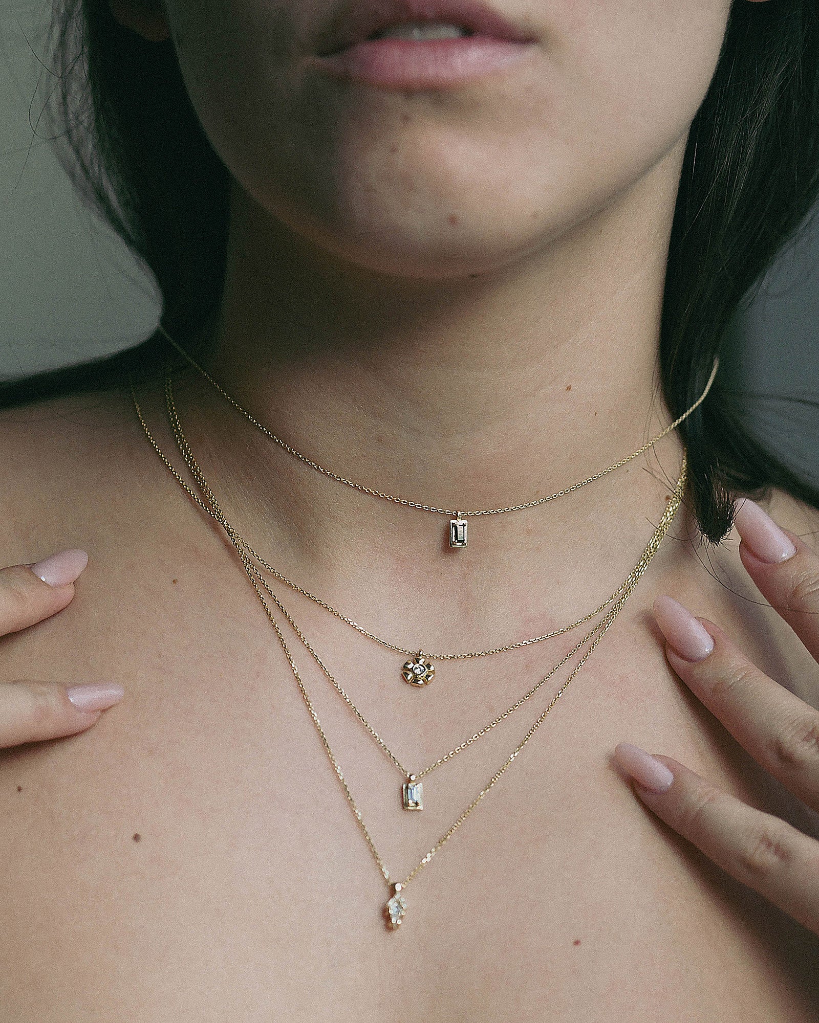 A person wearing a layered gold necklace with geometric black diamond pendants.