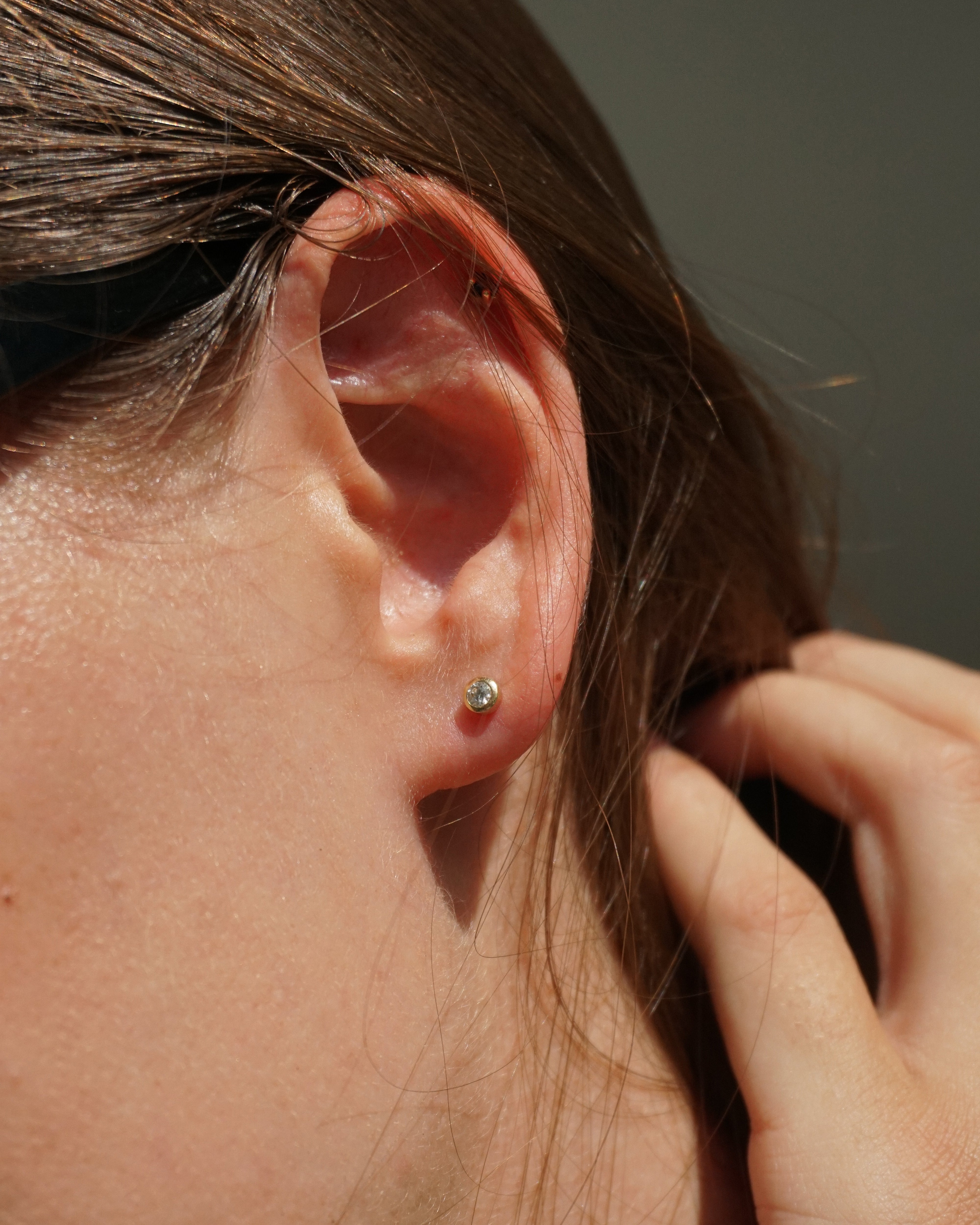 Close-up of an ear with a small earring, hand adjusting hair