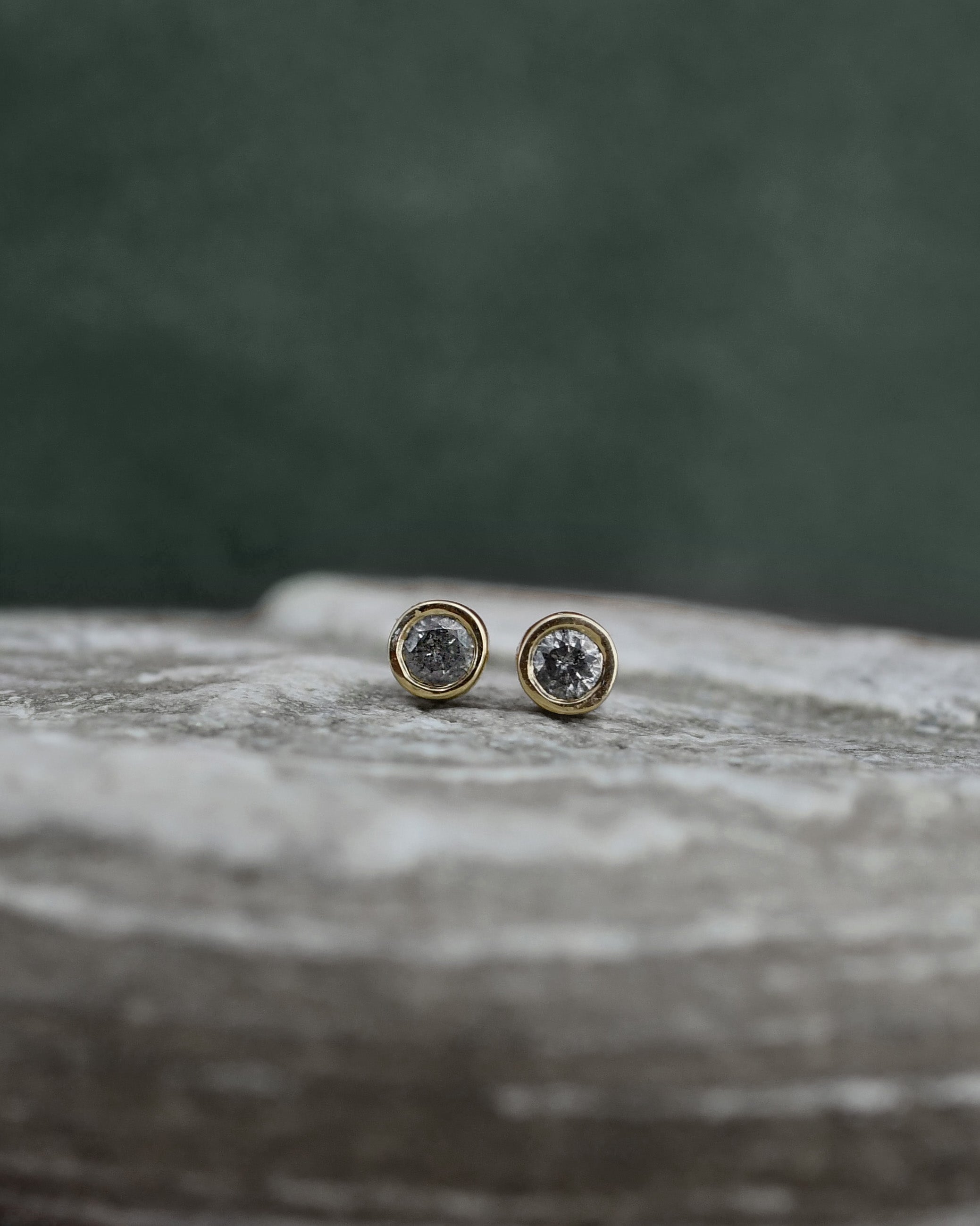 Pair of stud dark gray diamond earrings displayed on a marble slab against 
