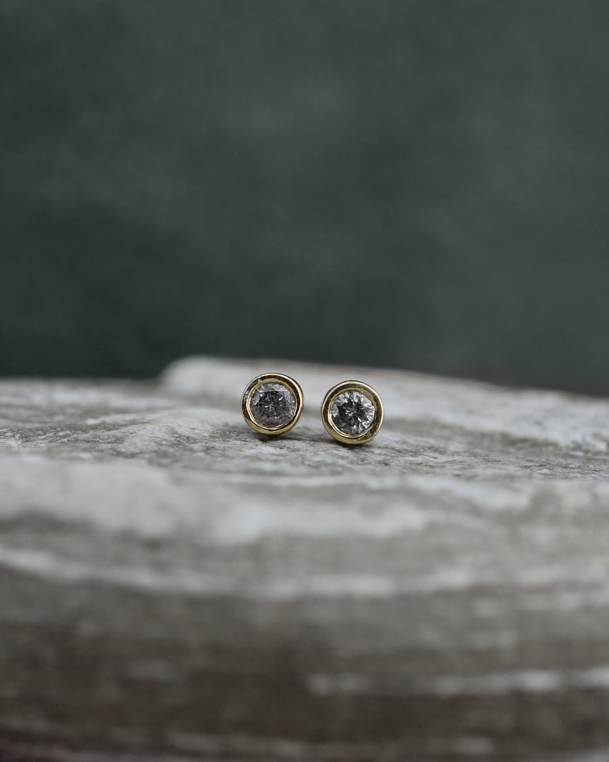 Pair of stud dark gray diamond earrings displayed on a marble slab against 