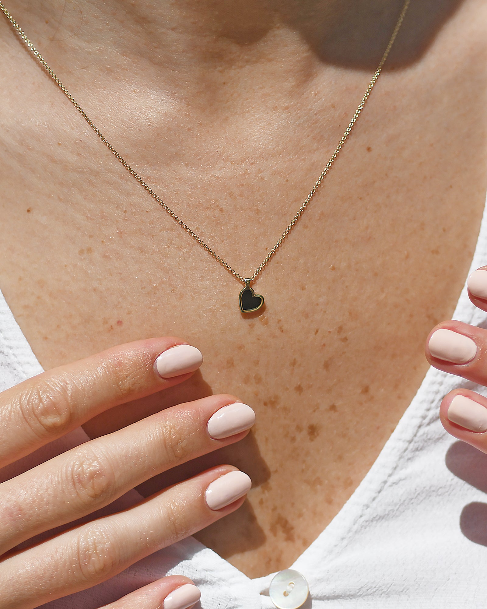 Gold necklace with a heart pendant on a person's neck, close-up view.