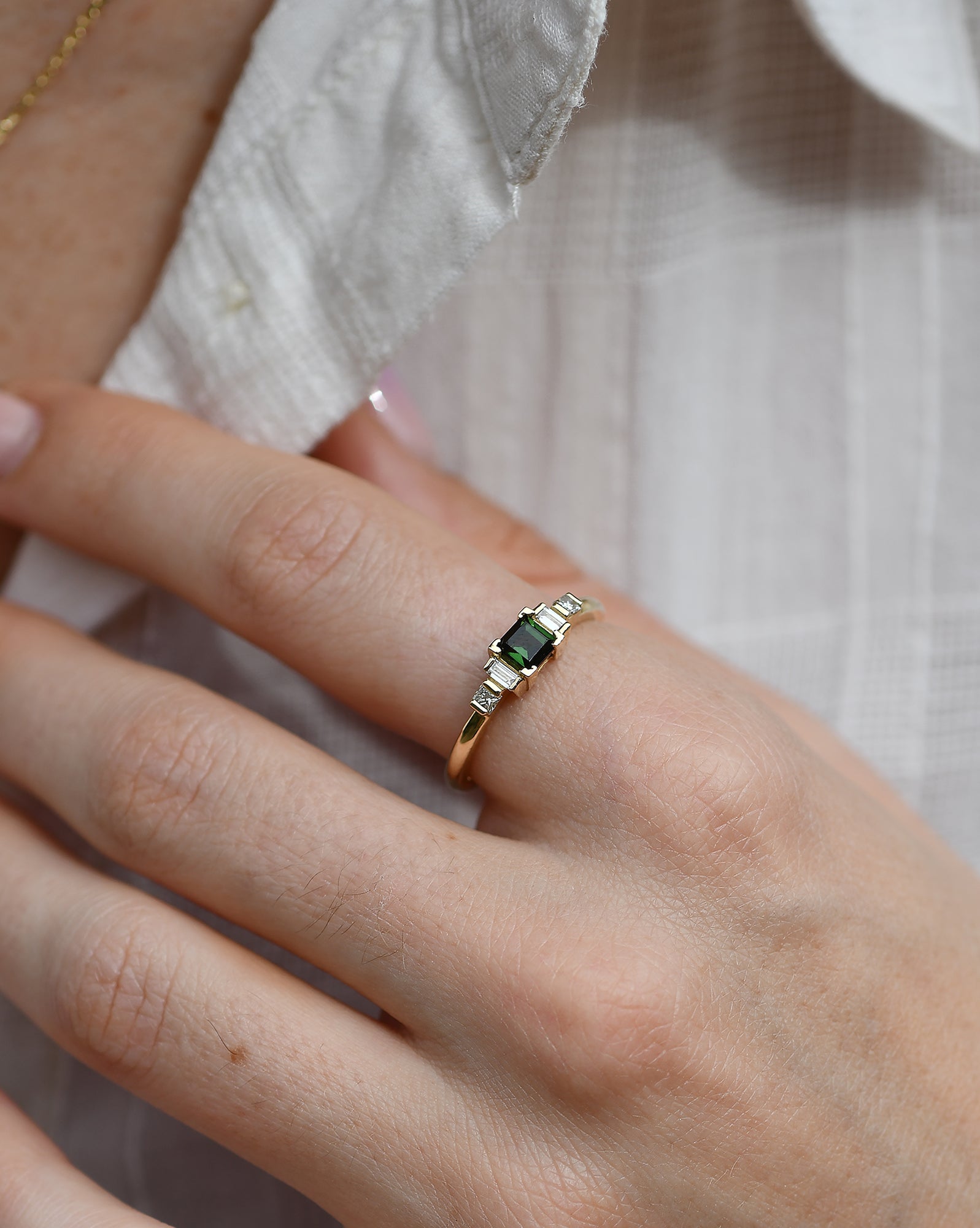 A gold ring featuring a square-cut green tourmaline center stone flanked by two baguette-cut diamonds