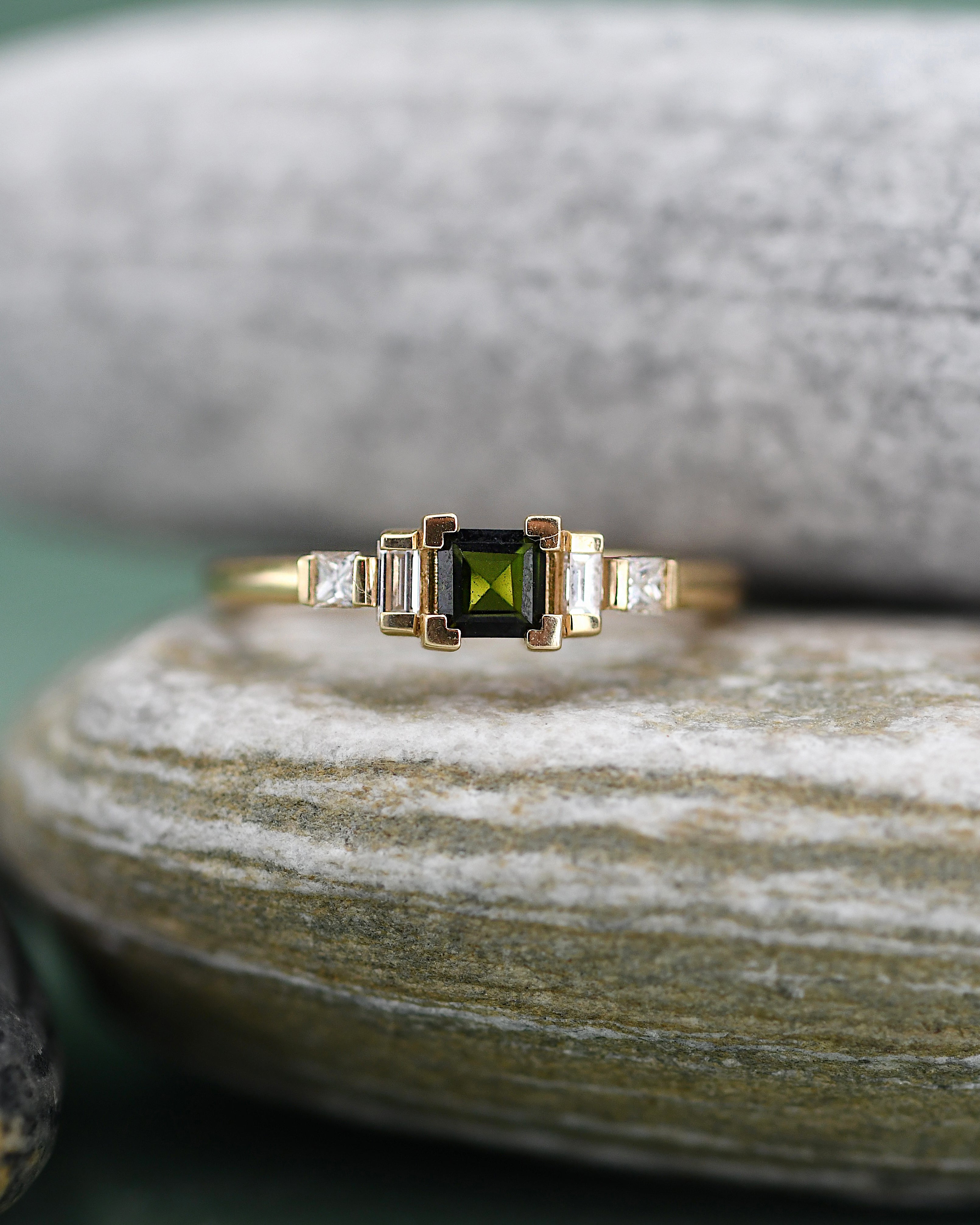 A gold ring featuring a square-cut green tourmaline center stone flanked by two baguette-cut diamonds