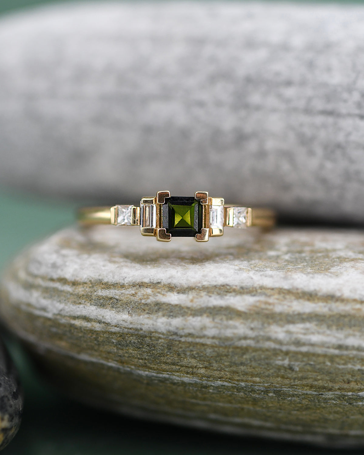 A gold ring featuring a square-cut green tourmaline center stone flanked by two baguette-cut diamonds