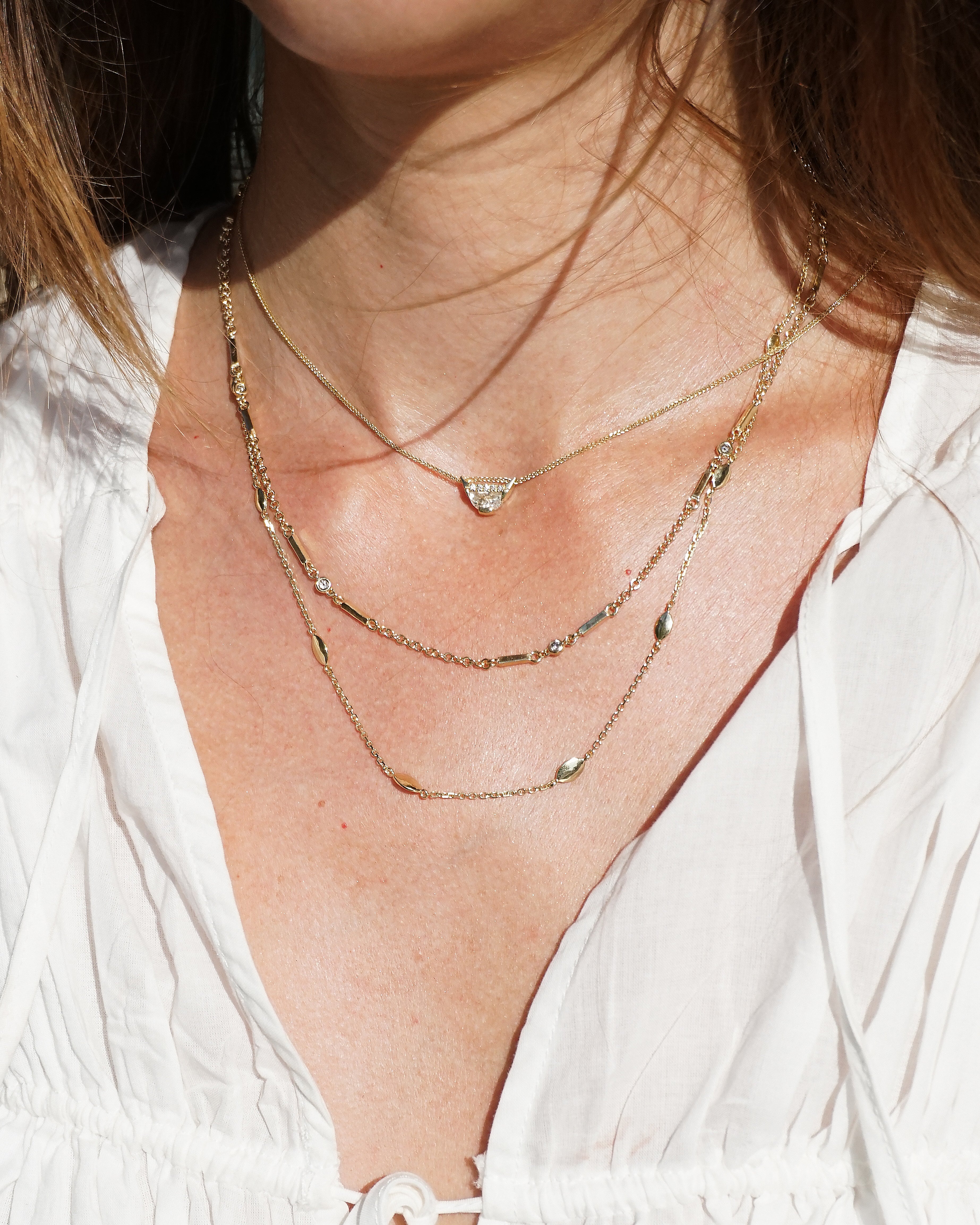 Close-up of a person wearing multiple gold necklaces with a white top.