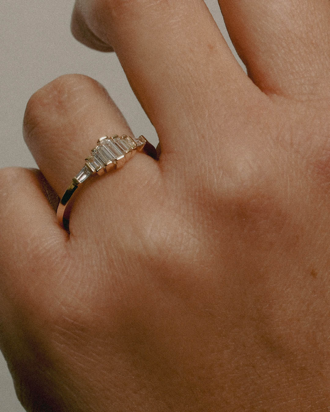 A hand wearing a gold ring with white diamond accents.