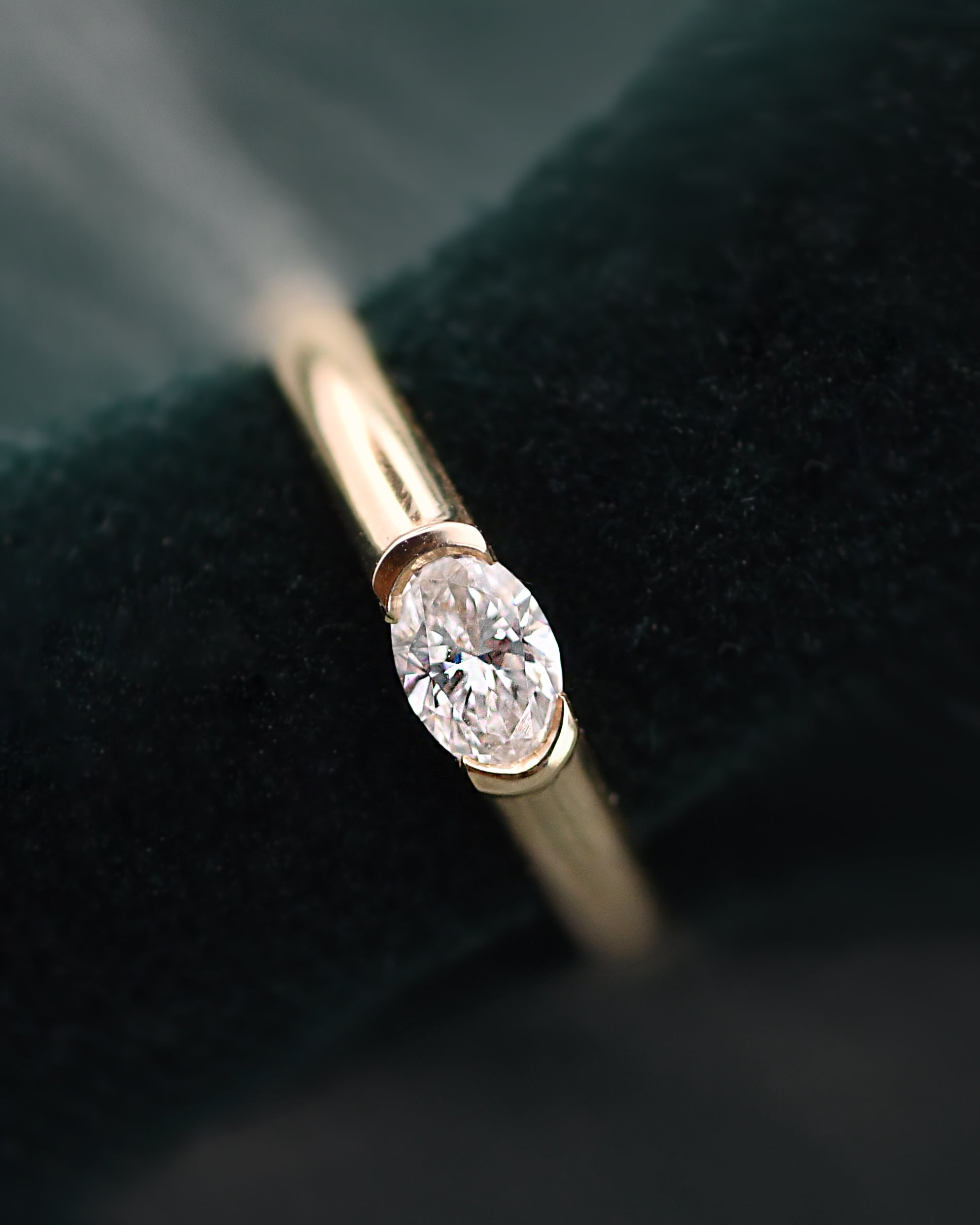 An oval-cut diamond ring, displayed on a dark green velvet ring stand.