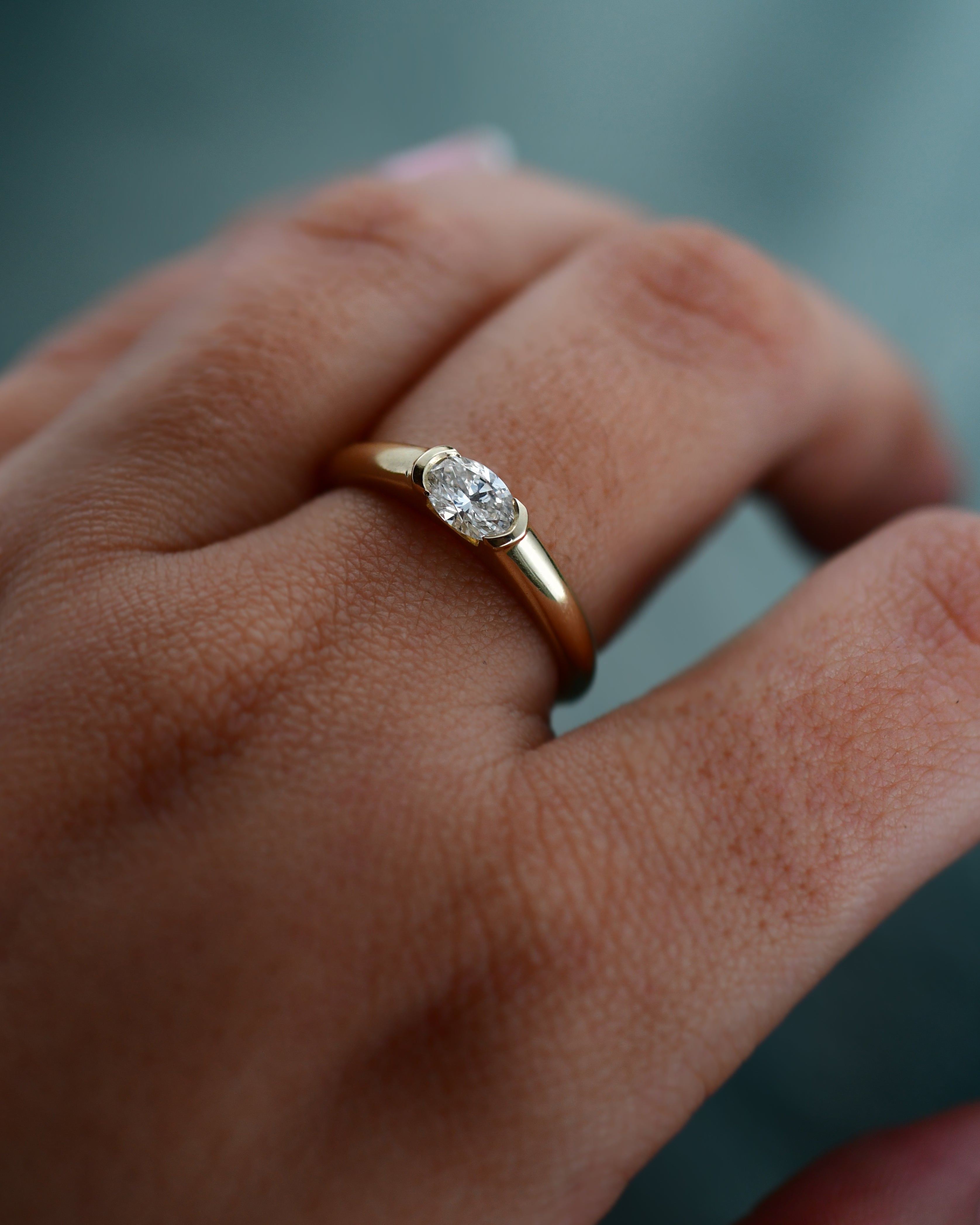 A close-up of a hand wearing a yellow gold ring with an oval-cut clear diamond