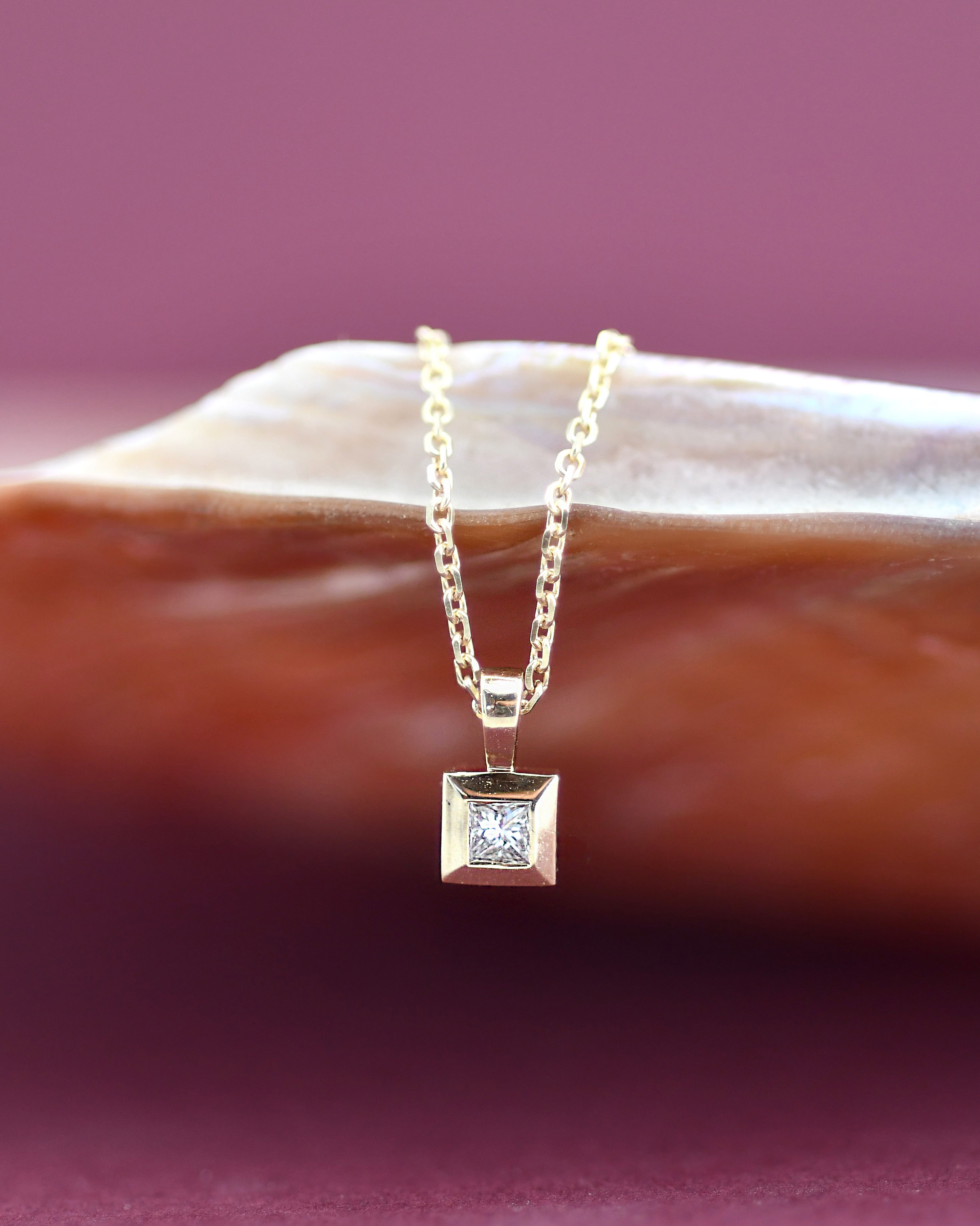 Gold necklace with a square diamond pendant on a pink background
