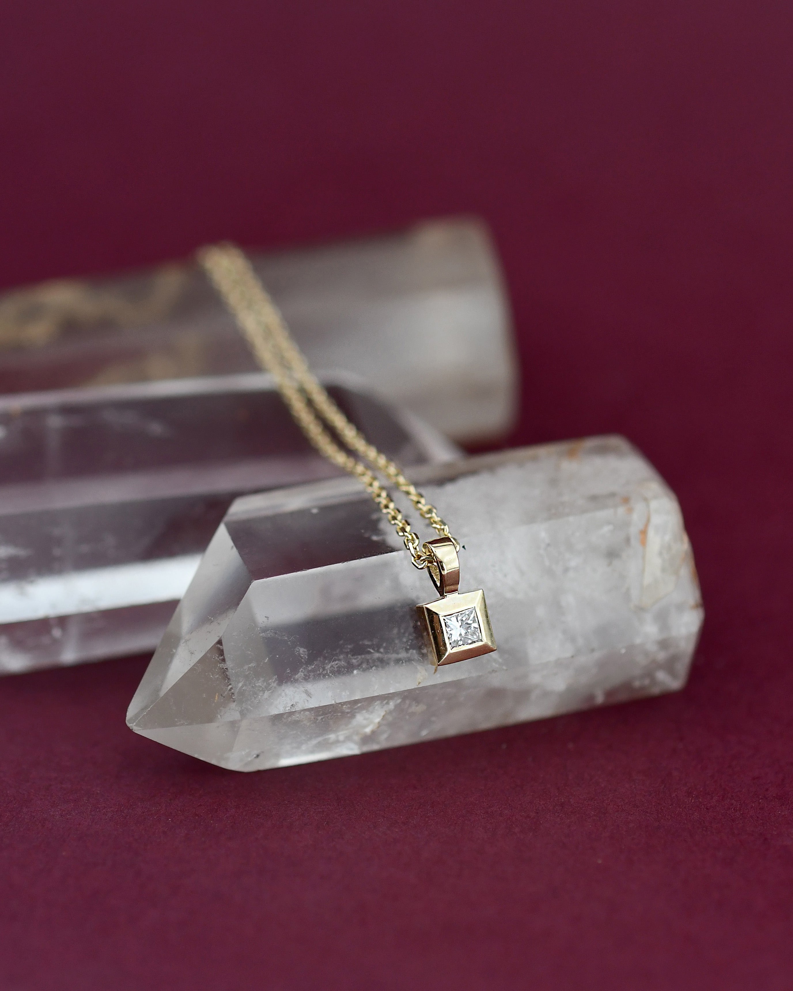 Gold necklace with a diamond pendant on a crystal base against a red background