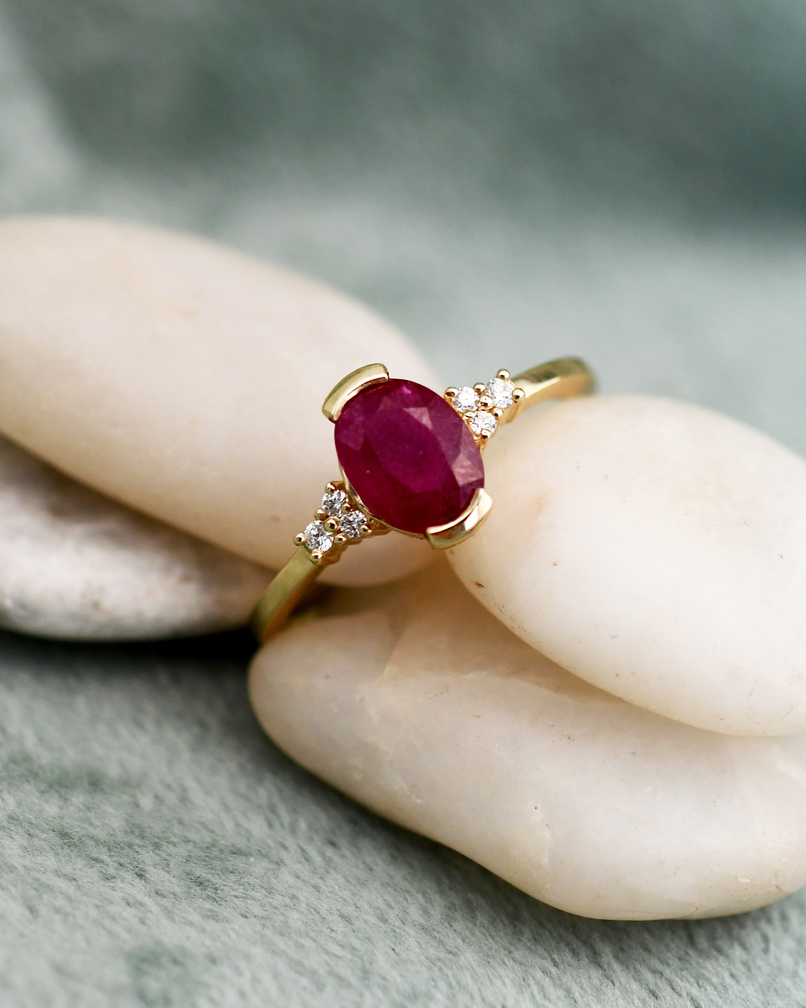 A gold ring with an oval deep red ruby center stone and small clear diamonds, 