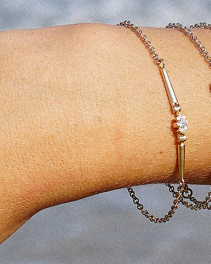 Gold bracelet with a diamond on a wrist against a neutral background