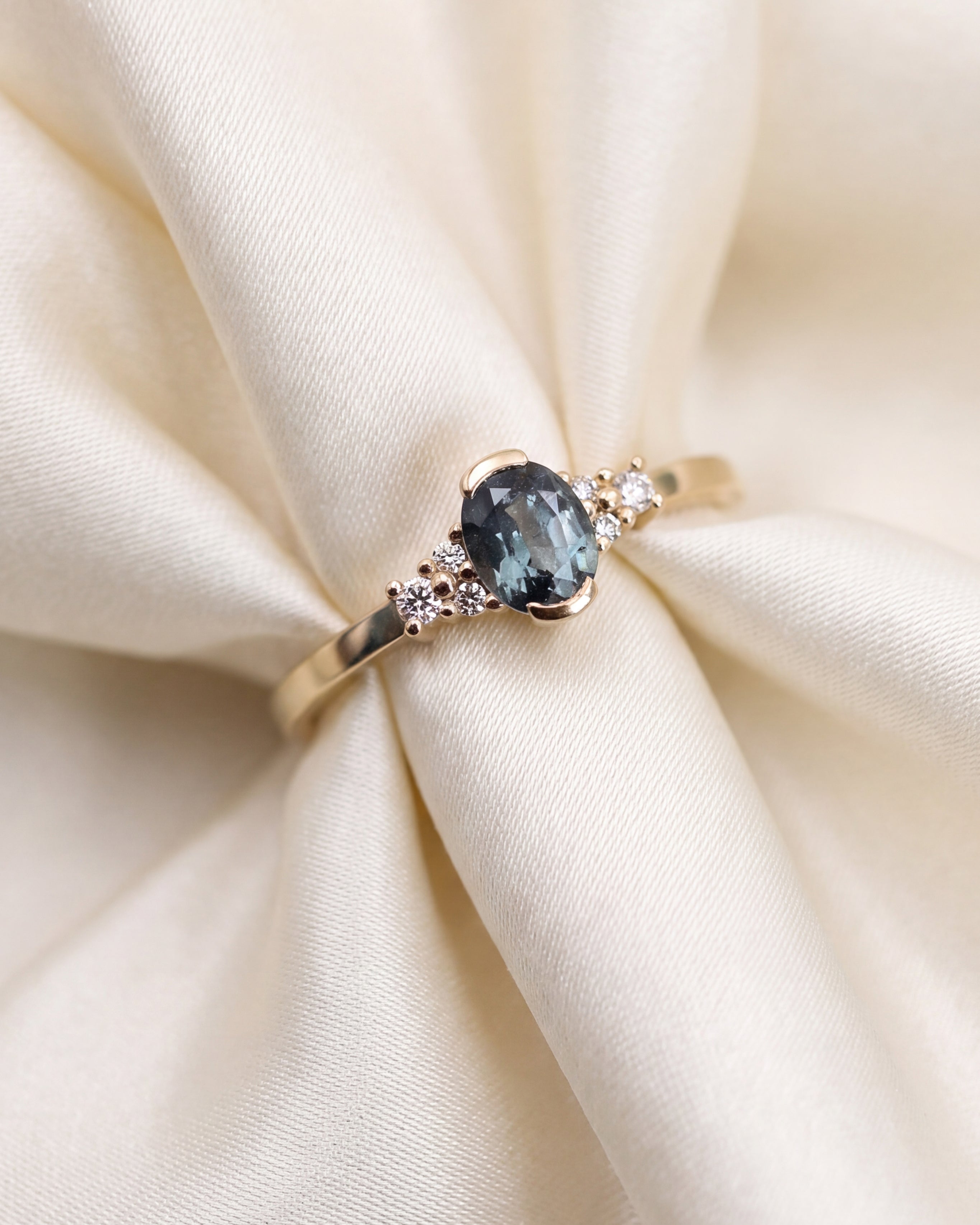 A yellow gold ring featuring a central oval-cut green sapphire gemstone accented by small round clear diamonds on either side, set against a plain white background.