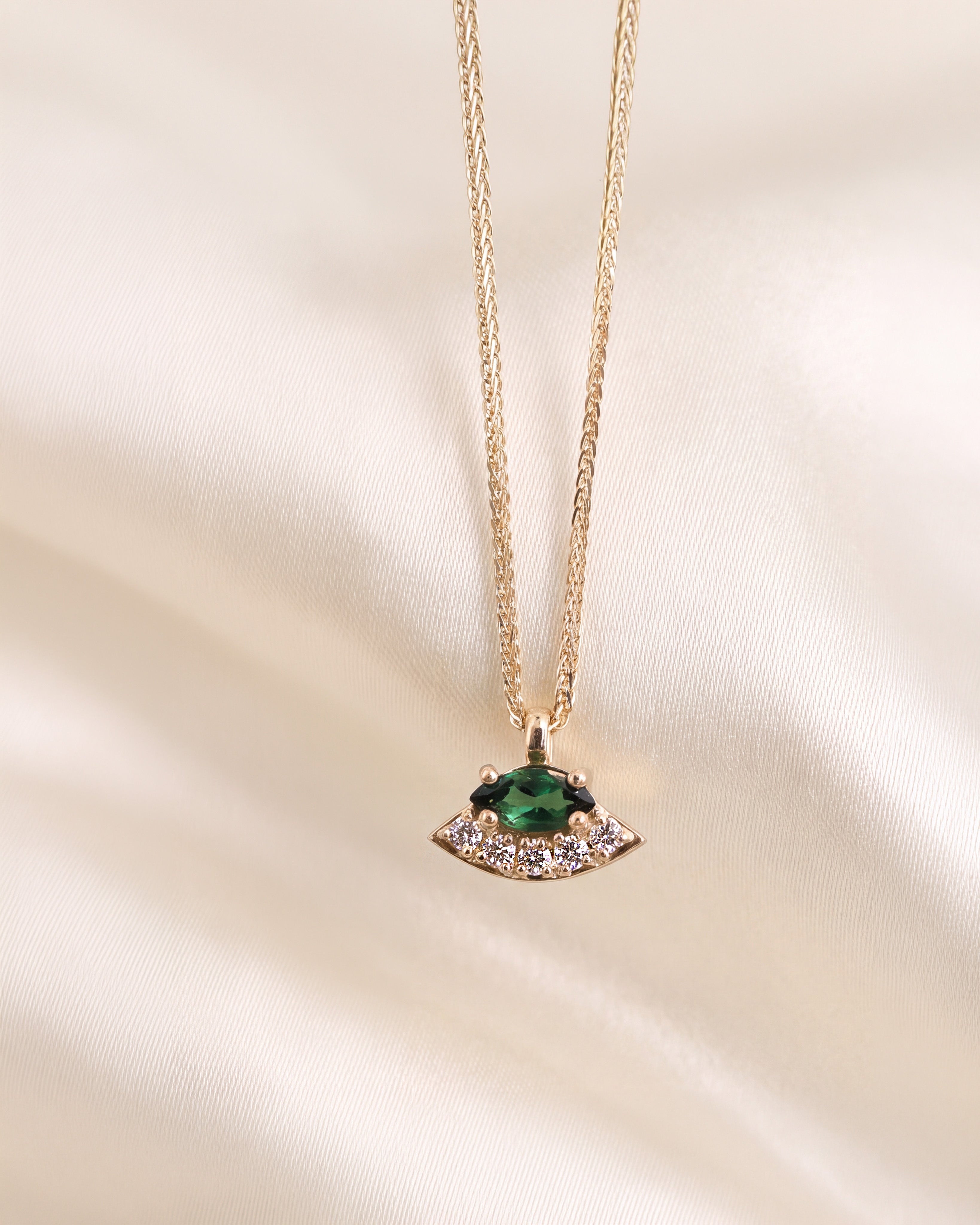 A gold pendant necklace with a green oval gemstone and small clear diamonds, displayed on a white background.