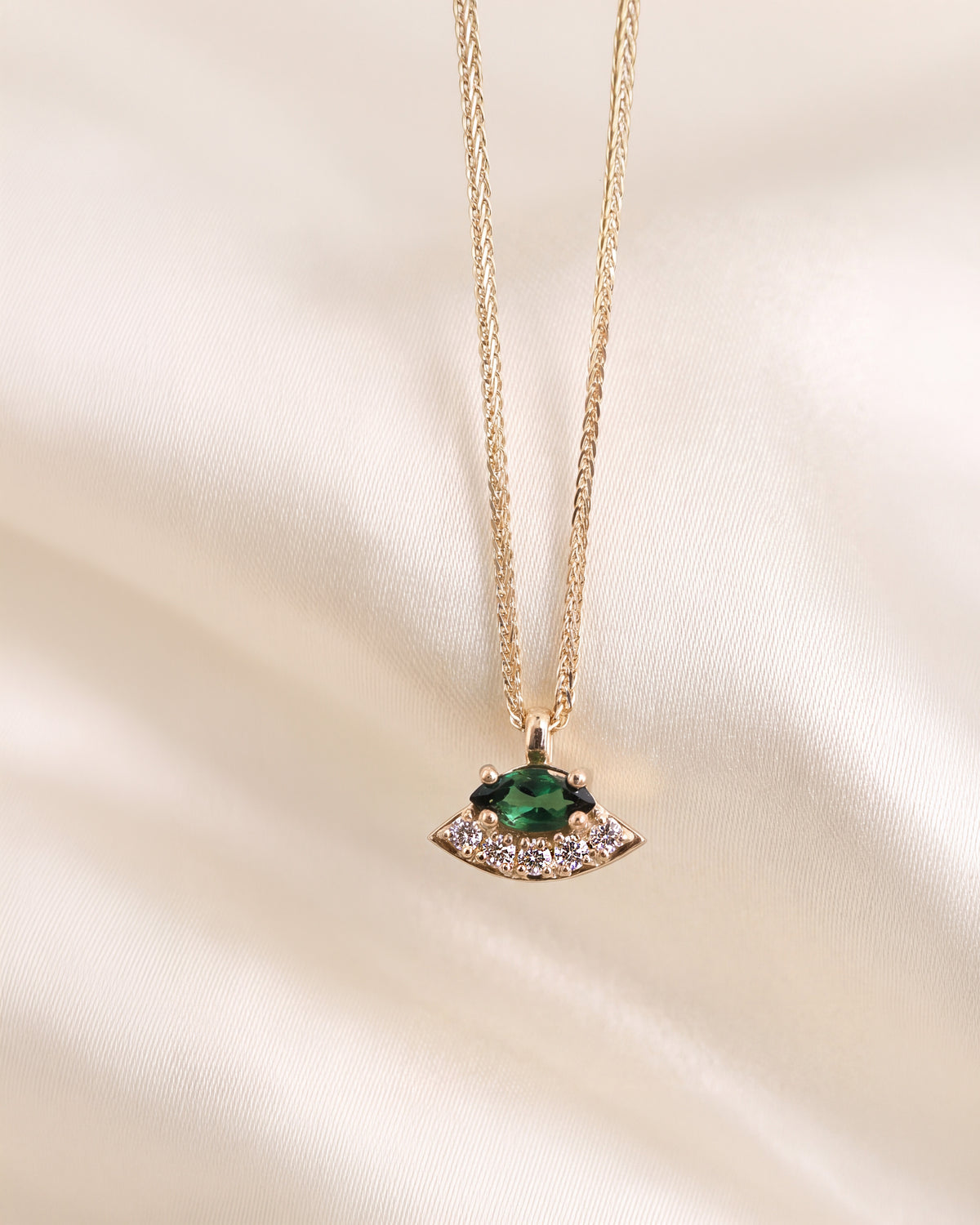 A gold pendant necklace with a green oval gemstone and small clear diamonds, displayed on a white background.