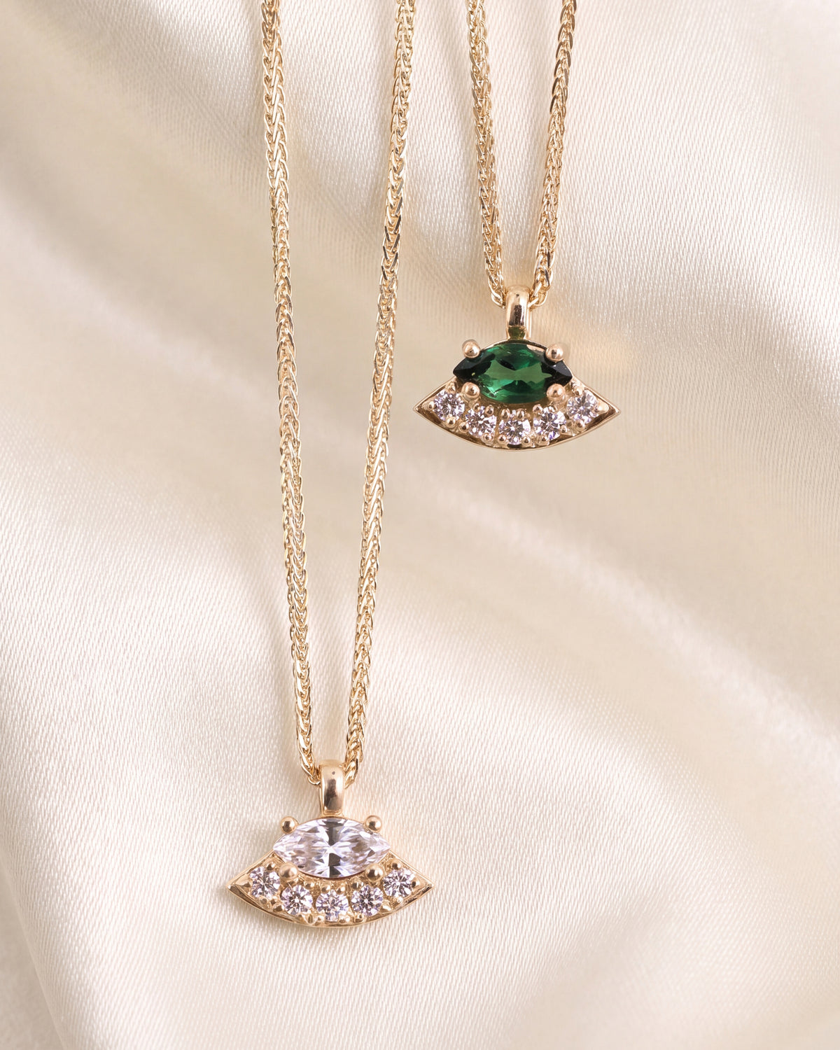 two gold pendant necklaces with a main marquis-cut main diamond and green gemstone, with small white diamonds below.