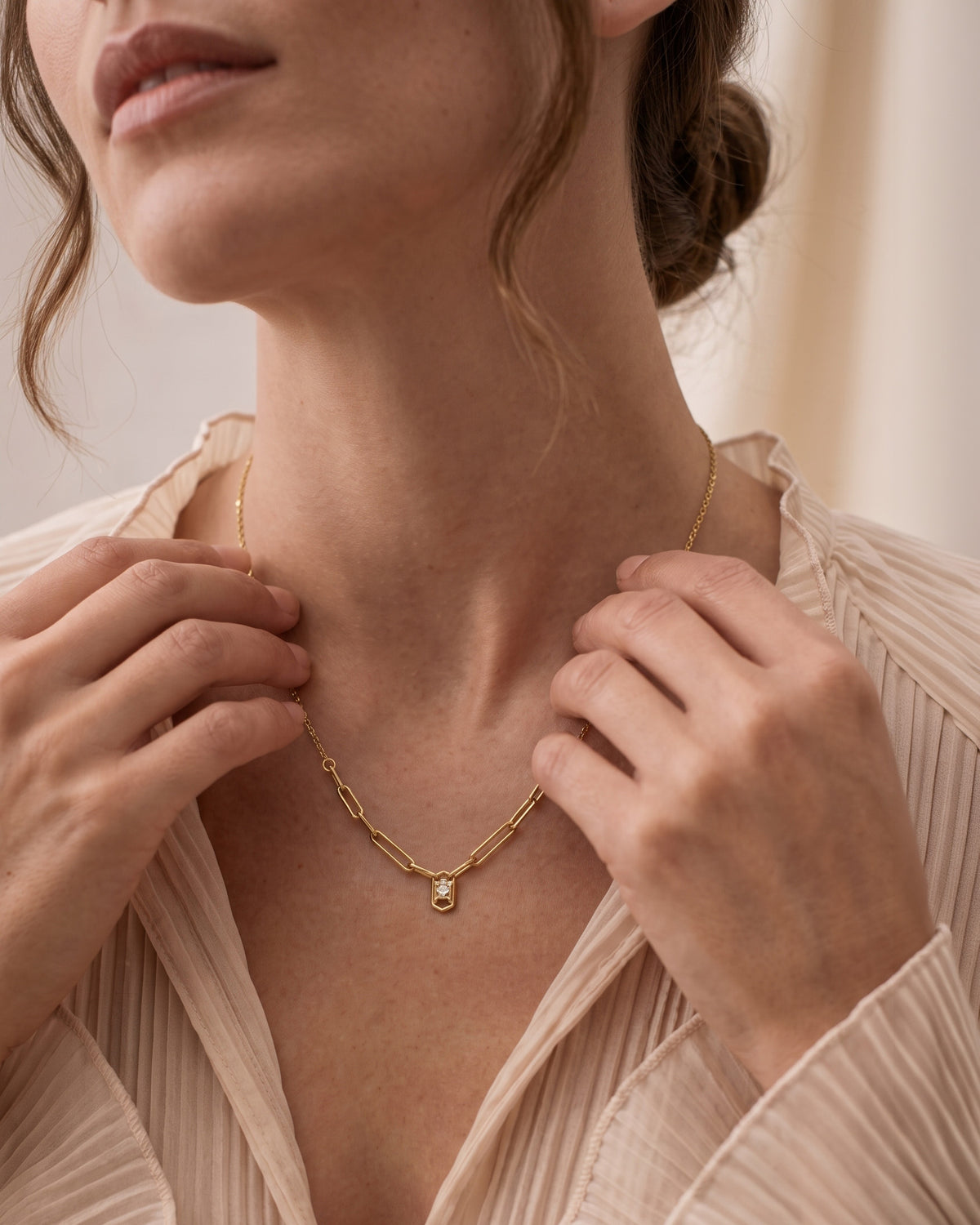 Woman  wears A gold chain necklace featuring a geometric link design that converges into a central pendant frame holding a clear diamond