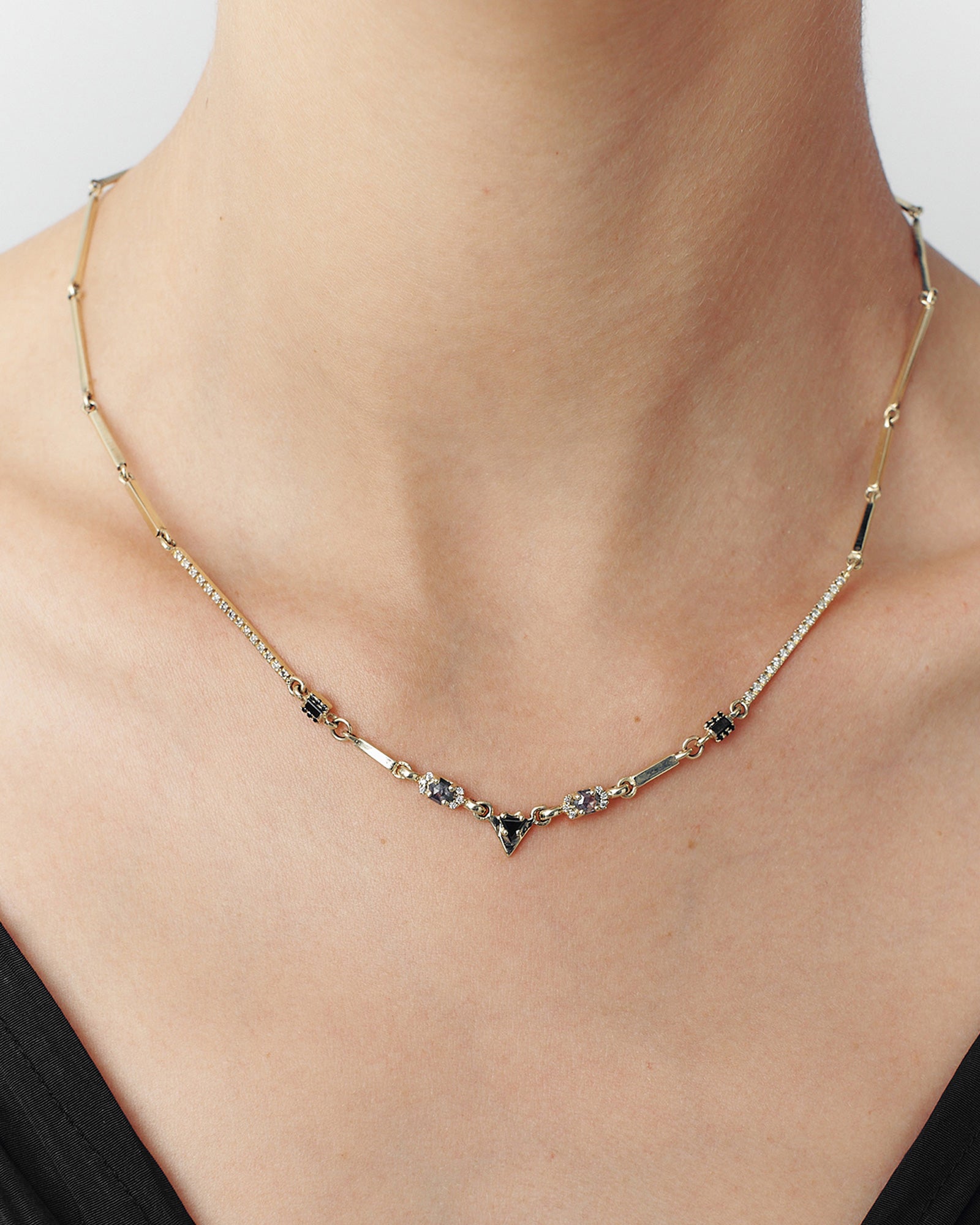 A person wearing a gold-colored necklace with black and grey diamond elements along the chain, showcasing an art deco style.